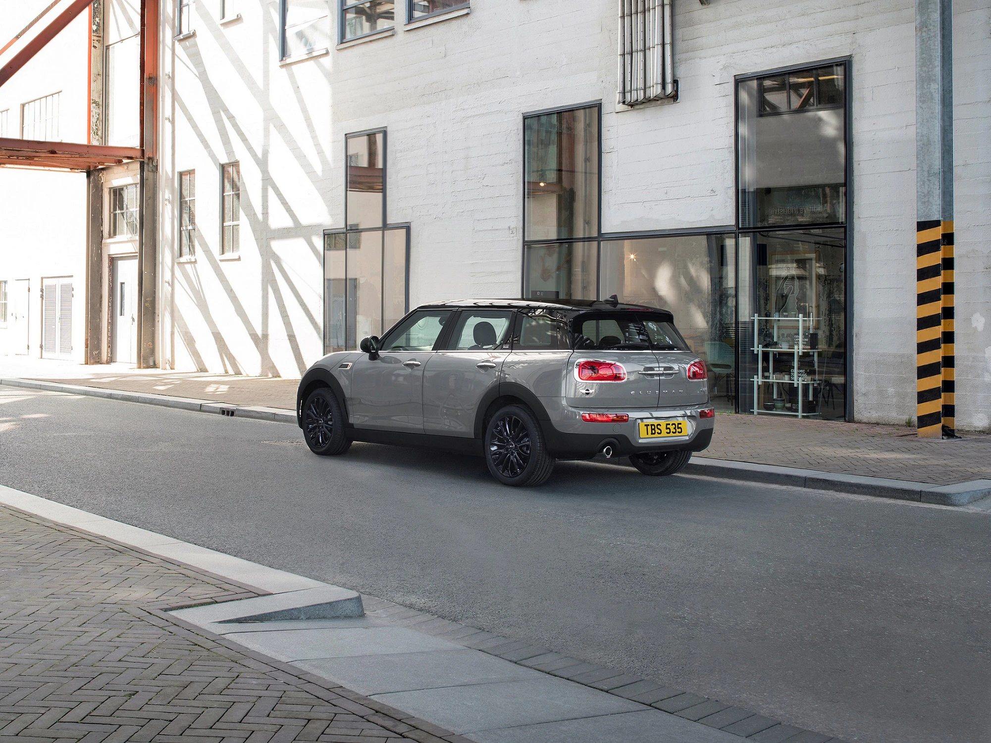 Silberner Kleinwagen parkt auf leerer städtischer Straße neben einem großen Gebäude aus Beton und Glas.