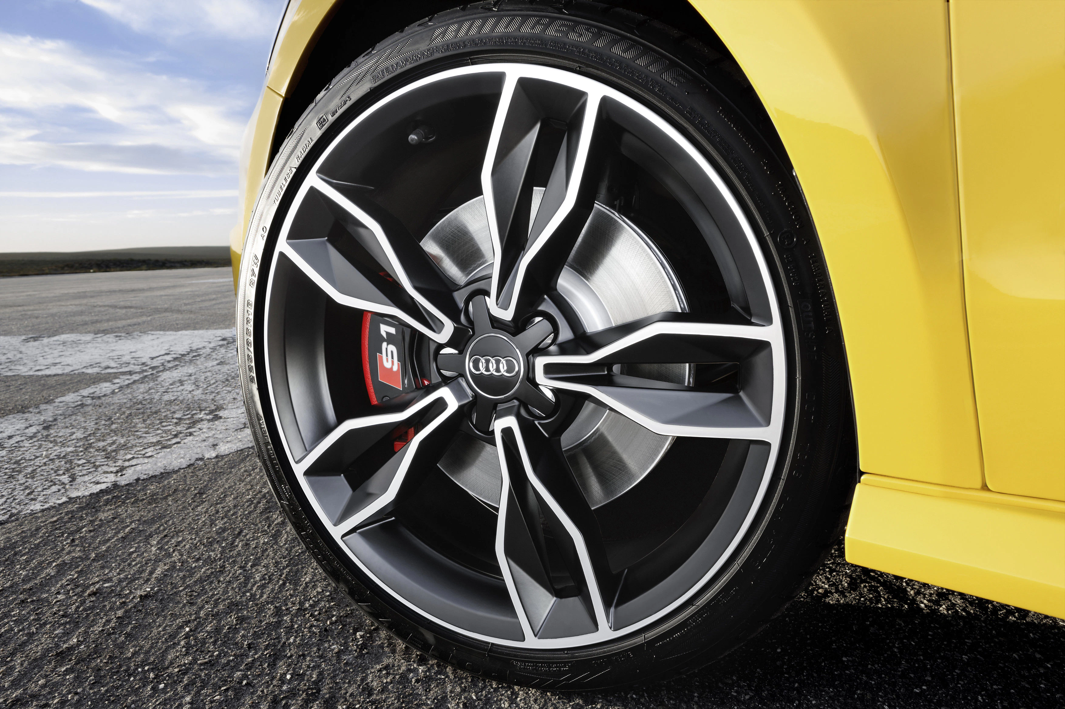 Nahaufnahme eines sportlichen Audi-Rads mit auffälligem Felgendesign und rotem Bremssattel auf einer Asphaltfläche in der Nähe der Natur.