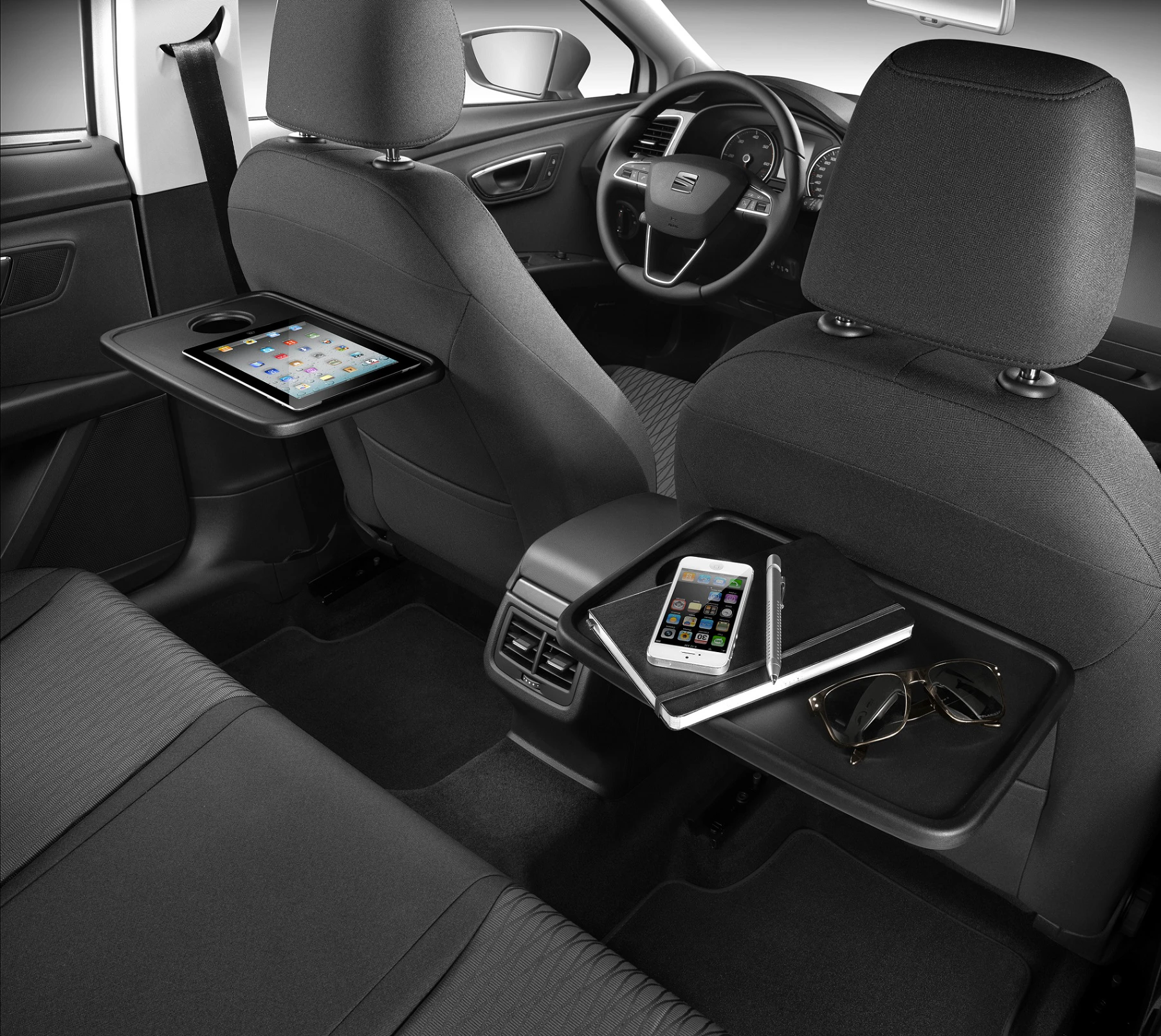 Auto-Innenraum mit Tabletts und Staufächern an den Rücksitzen: Tablet, Smartphone, Notizbuch, Stifte und Sonnenbrille sichtbar.