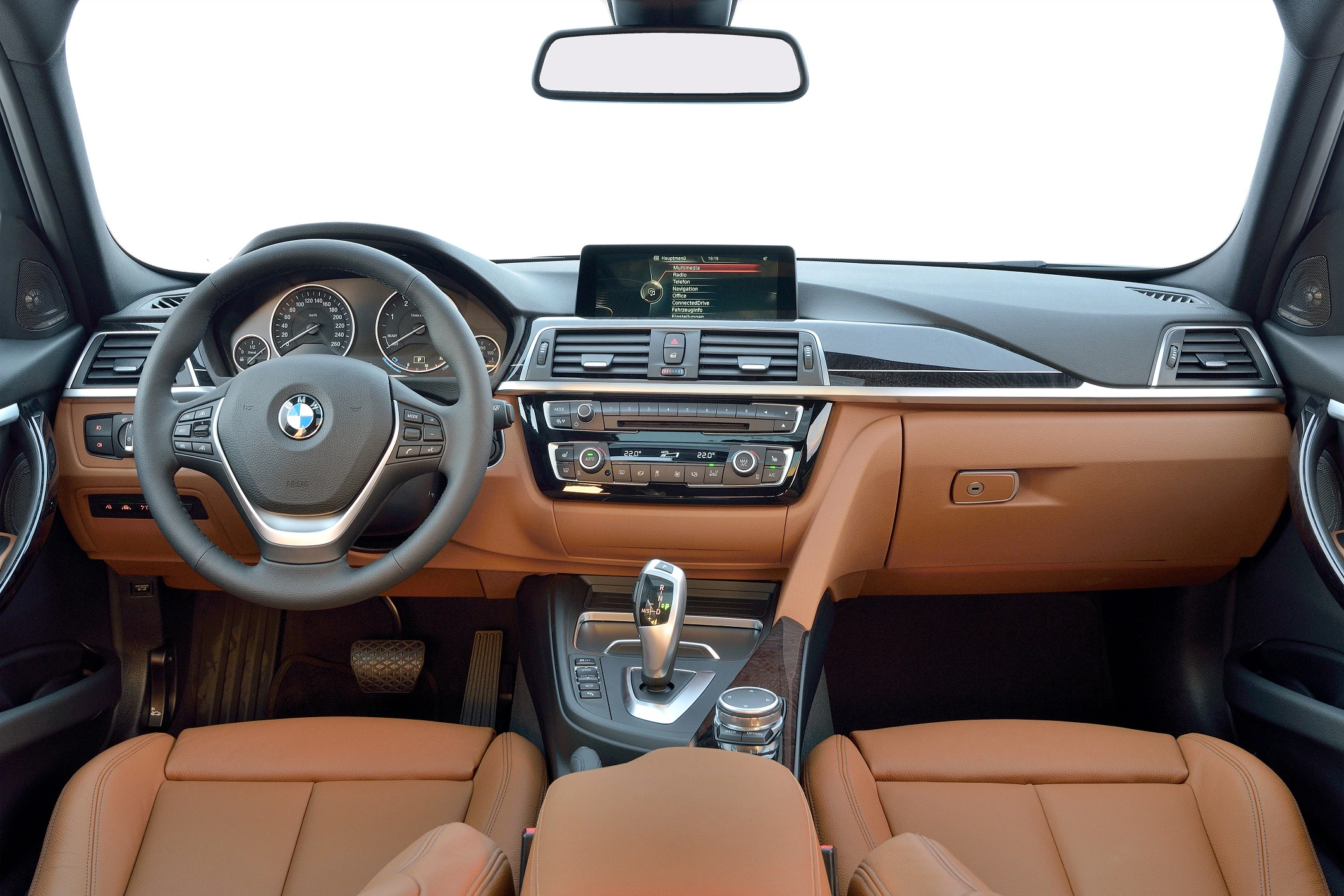 Innenraum eines Autos mit braunen Ledersitzen, zentralem Display und Lenkrad mit BMW-Logo. Schalter und Armaturen sind modern gestaltet.