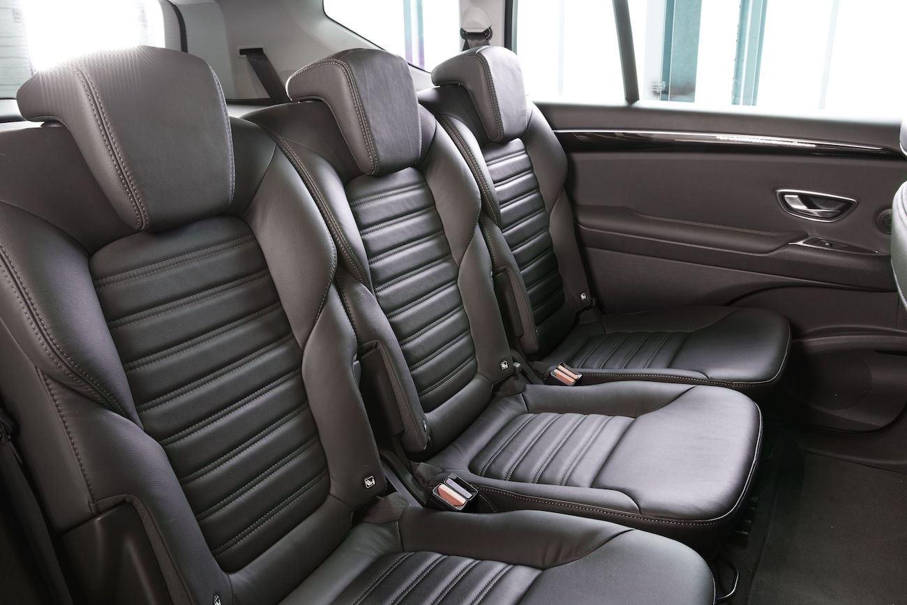 Dreireihige schwarze Ledersitze in einem Auto, geräumig und modern, mit nach unten geklappten Kopflehnen und grauen Nähten.