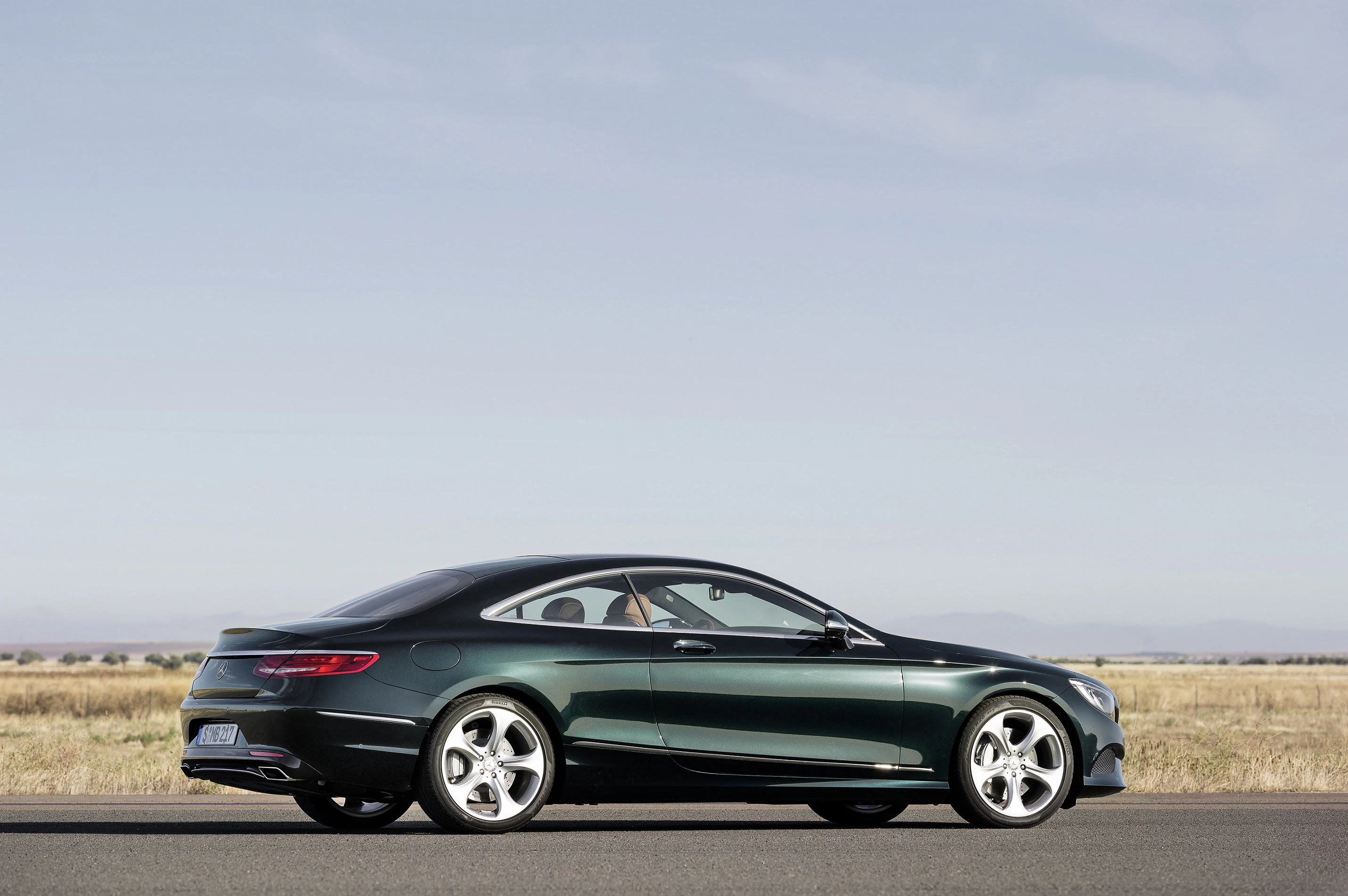 Grünes Coupé-Auto auf einer Landstraße mit weitem, wolkenlosem Himmel und offener Graslandschaft im Hintergrund.