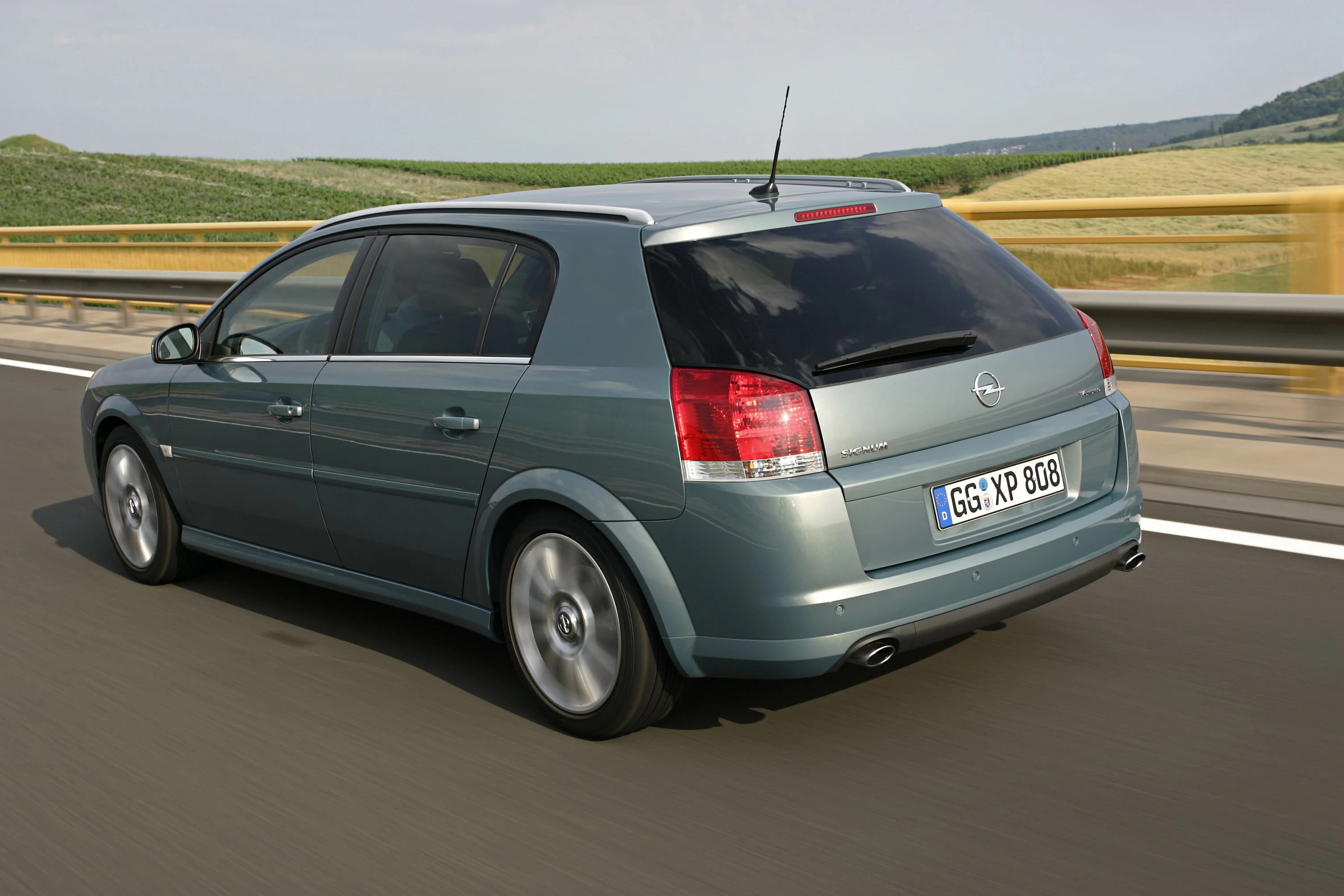 Grüner Opel Astra fährt auf einer Landstraße mit verschwommener Landschaft im Hintergrund.