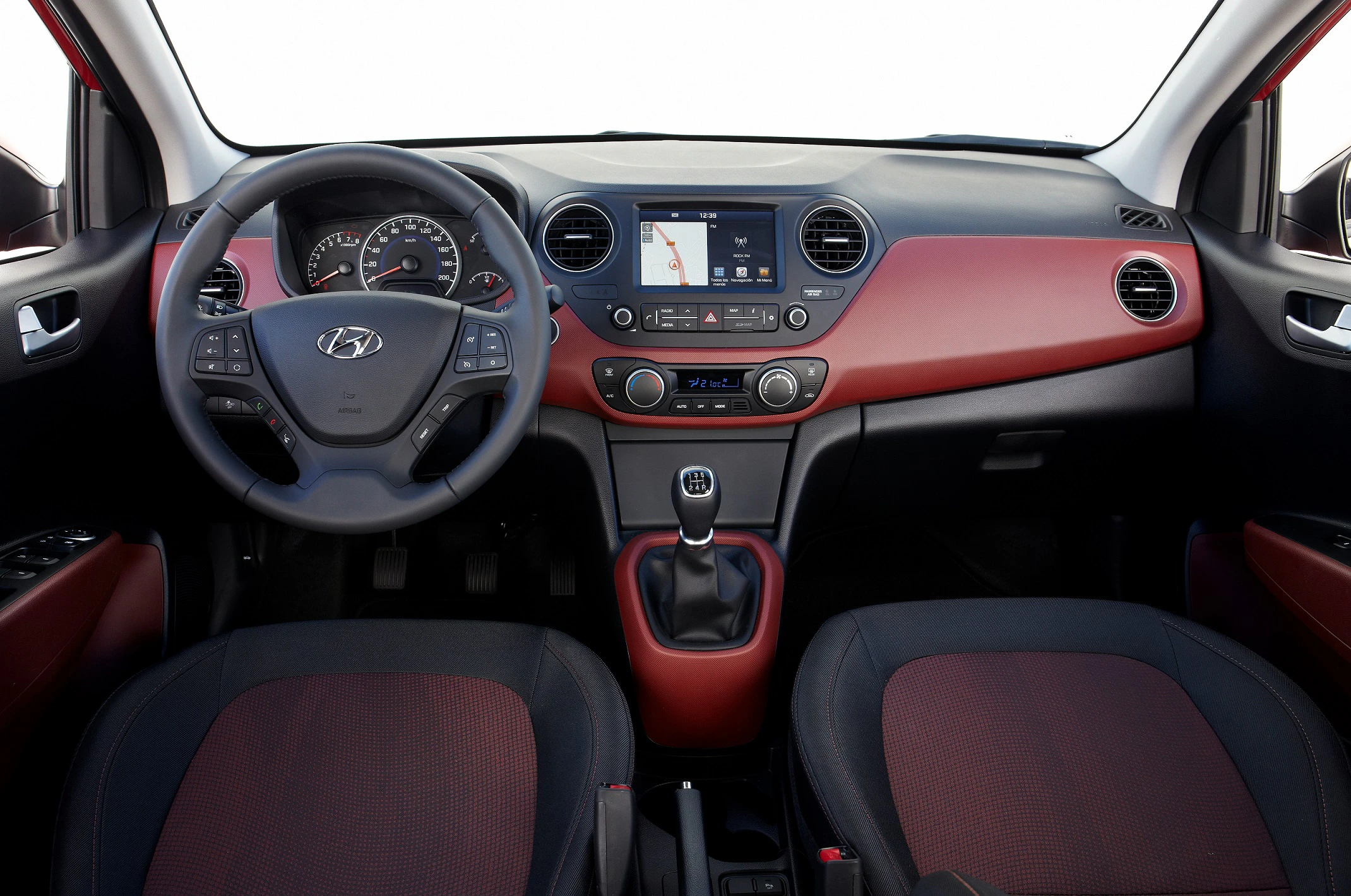 Lenkrad und Armaturenbrett eines Autos mit schwarzem und rotem Interieur, Touchscreen und manuellem Schalthebel.