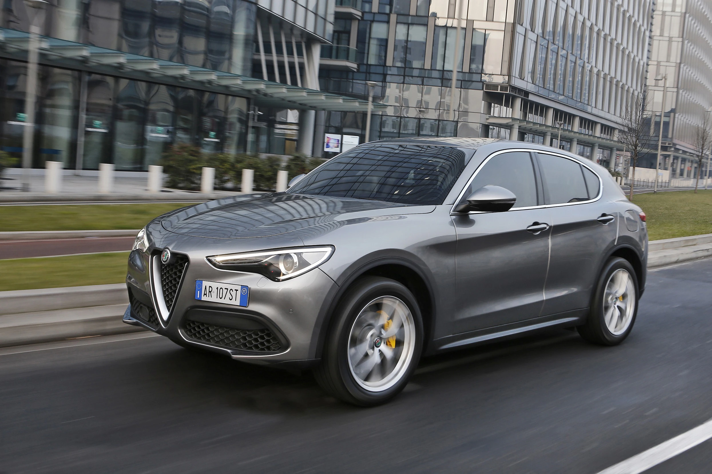 Silberner Alfa Romeo SUV fährt auf einer städtischen Straße, umgeben von modernen Glasgebäuden.
