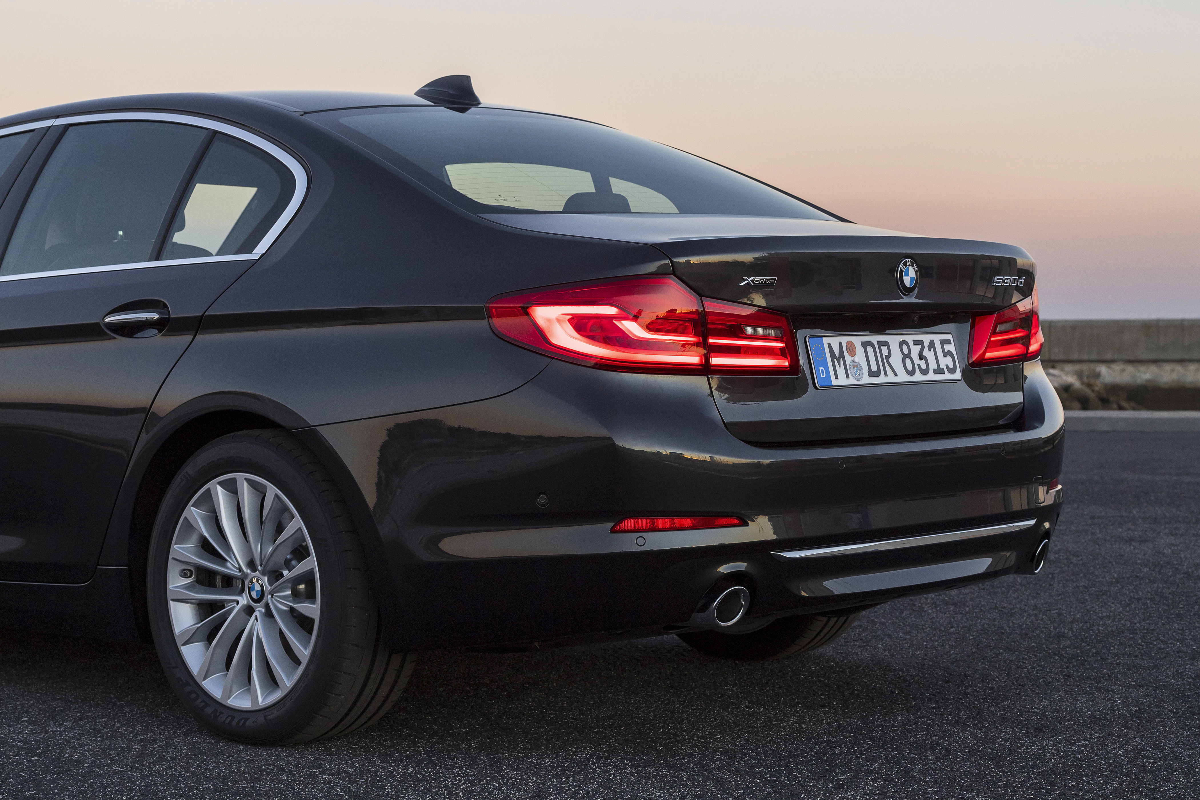 Schwarzer BMW 540i xDrive, Heckansicht bei Sonnenuntergang, auf einer Straße geparkt mit deutschen Nummernschildern.