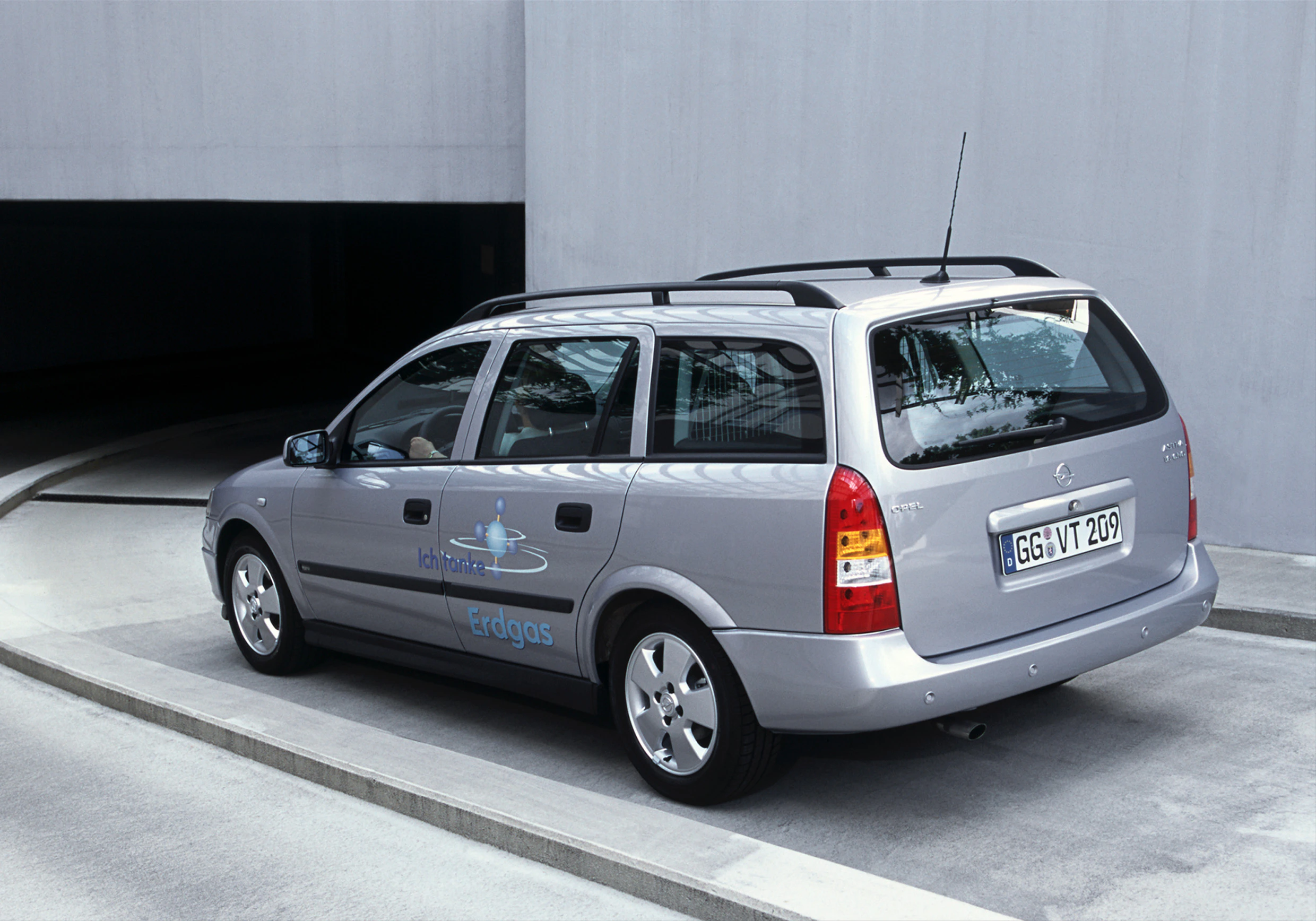 Silberner Kombi parkt auf einer Straße, markiert mit "Erdgas" und einem Logo auf der Seite, nahe einem dunklen Tunnel.