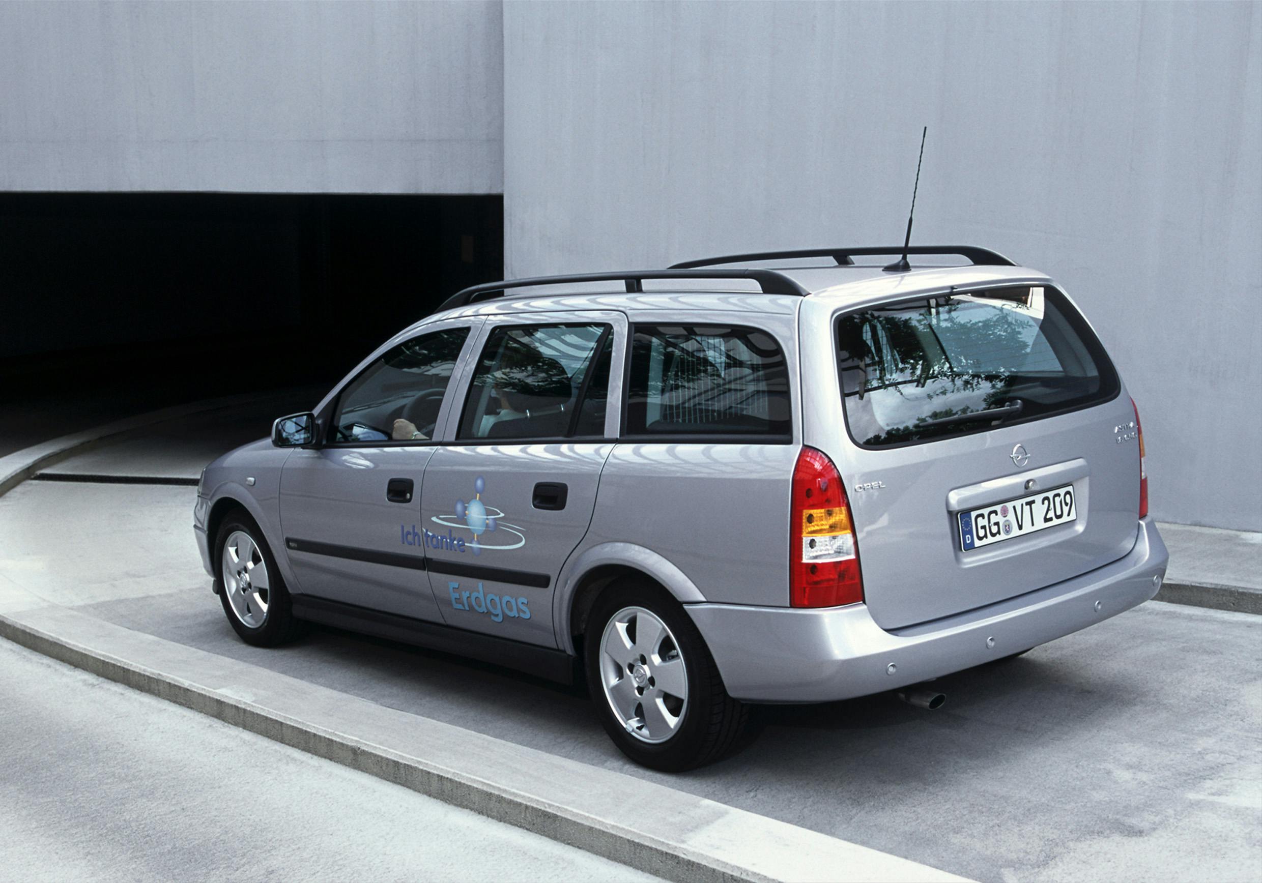 Silberner Kombi parkt auf einer Straße, markiert mit "Erdgas" und einem Logo auf der Seite, nahe einem dunklen Tunnel.
