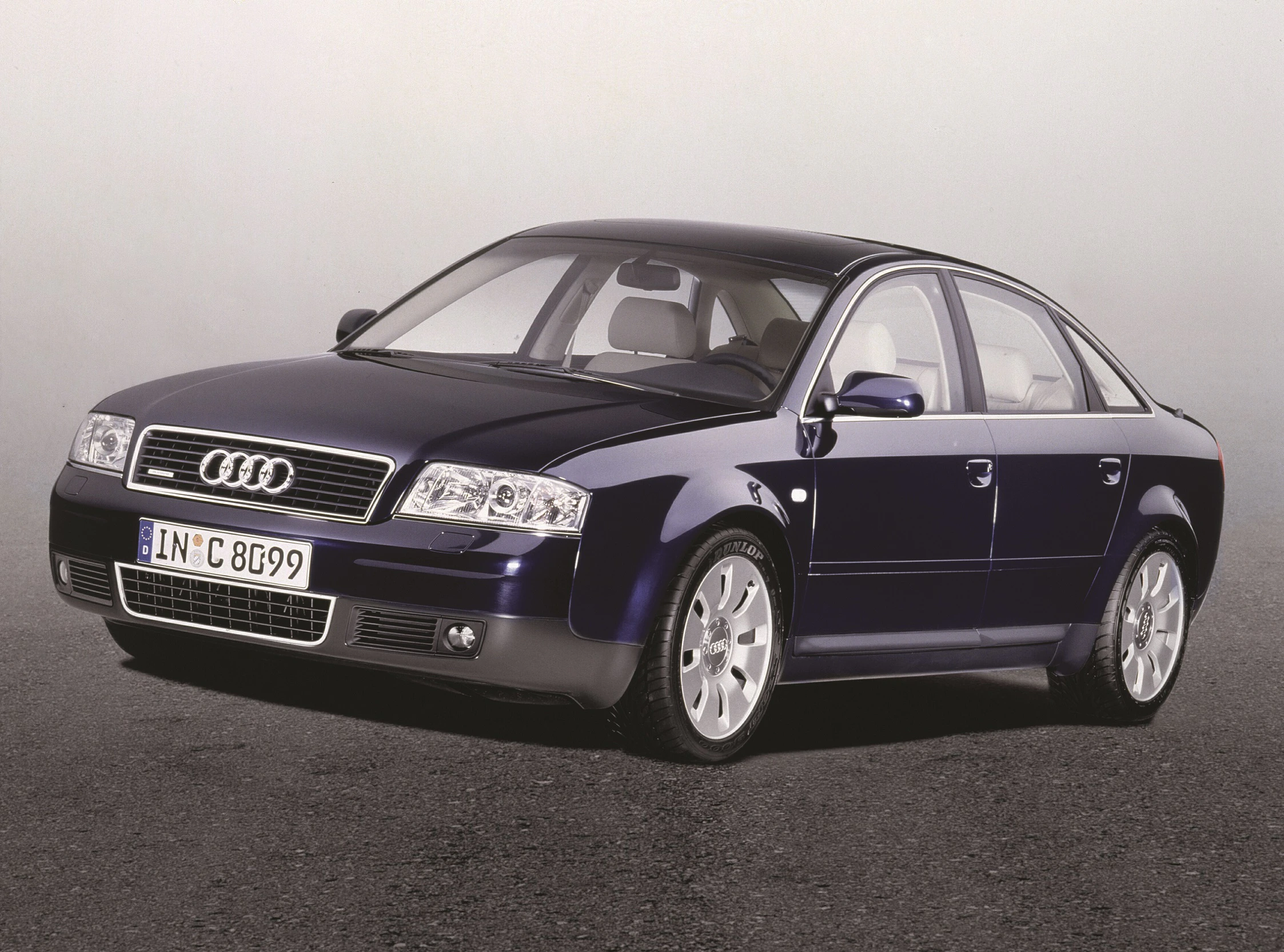 Dunkelblauer Audi A6 Limousine steht auf grauem Untergrund. Vorderansicht mit glänzendem Lack und markentypischem Kühlergrill.