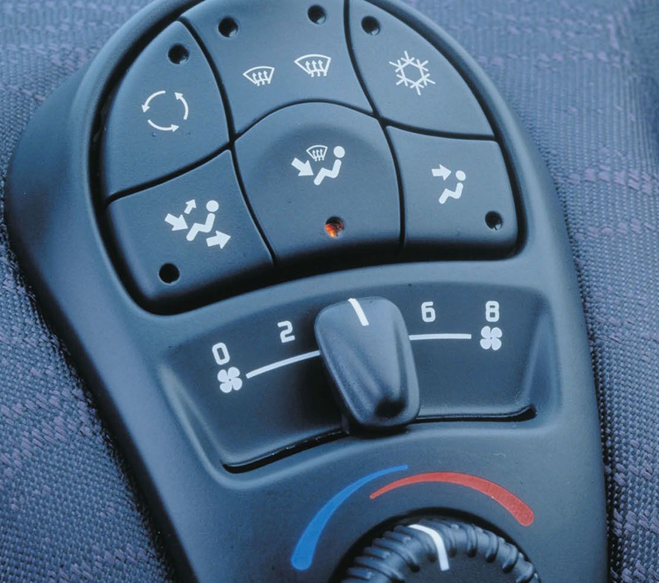 Nahaufnahme eines Fahrzeug-Klimaanlagen-Bedienfelds mit Drehregler, Symbolen für Lüftungsmodi und Temperaturanzeige in Blau und Rot.