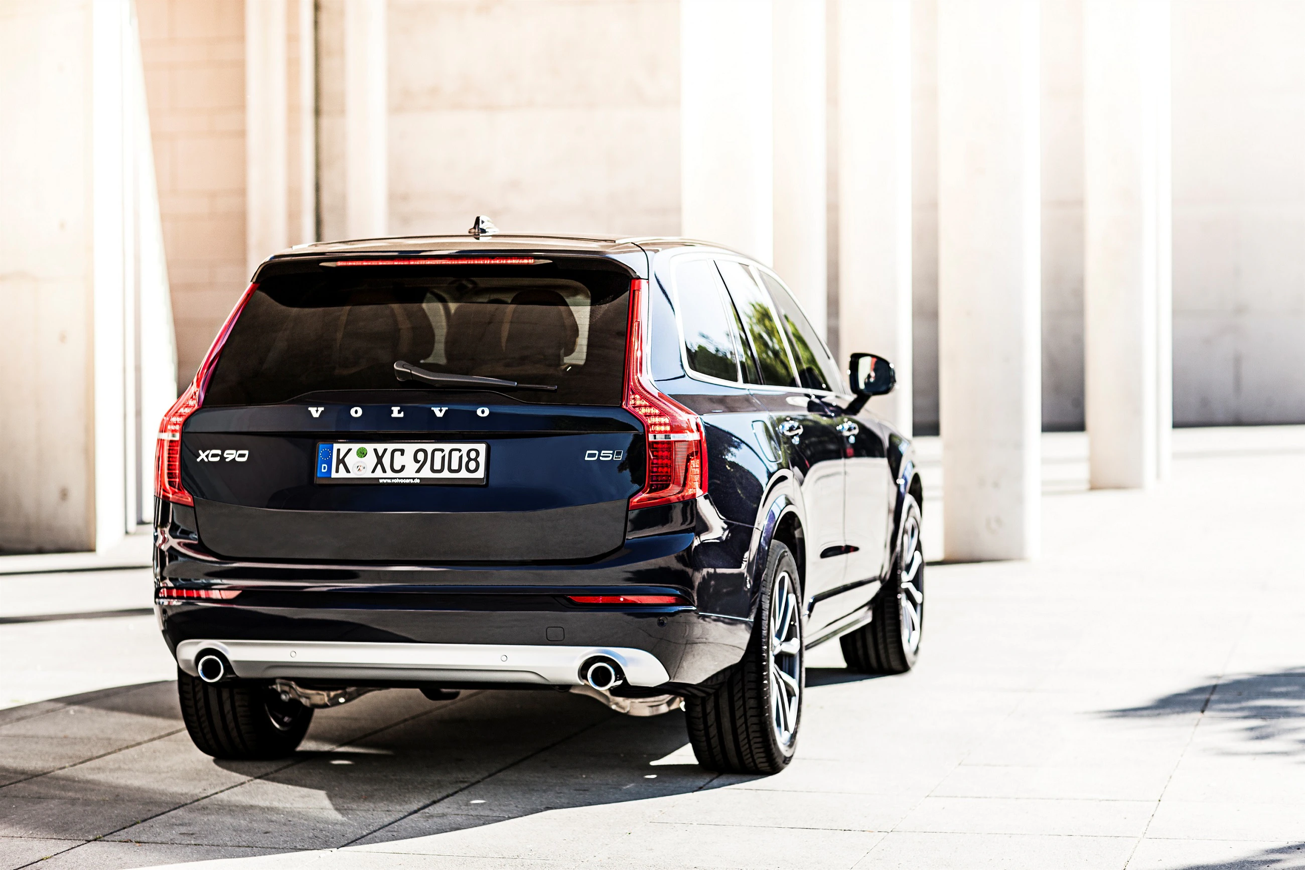 Schwarzer Volvo XC90 SUV parkt im Sonnenlicht auf einem modernen, grauen Stadtplatz.