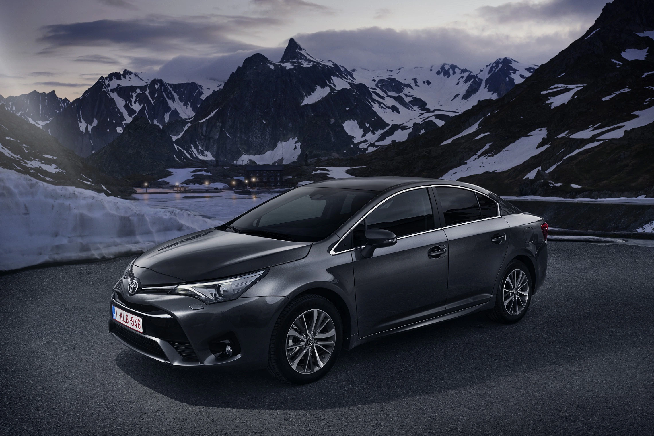 Dunkelgrauer Toyota vor schneebedeckten Bergen und bewölktem Himmel bei Dämmerung.