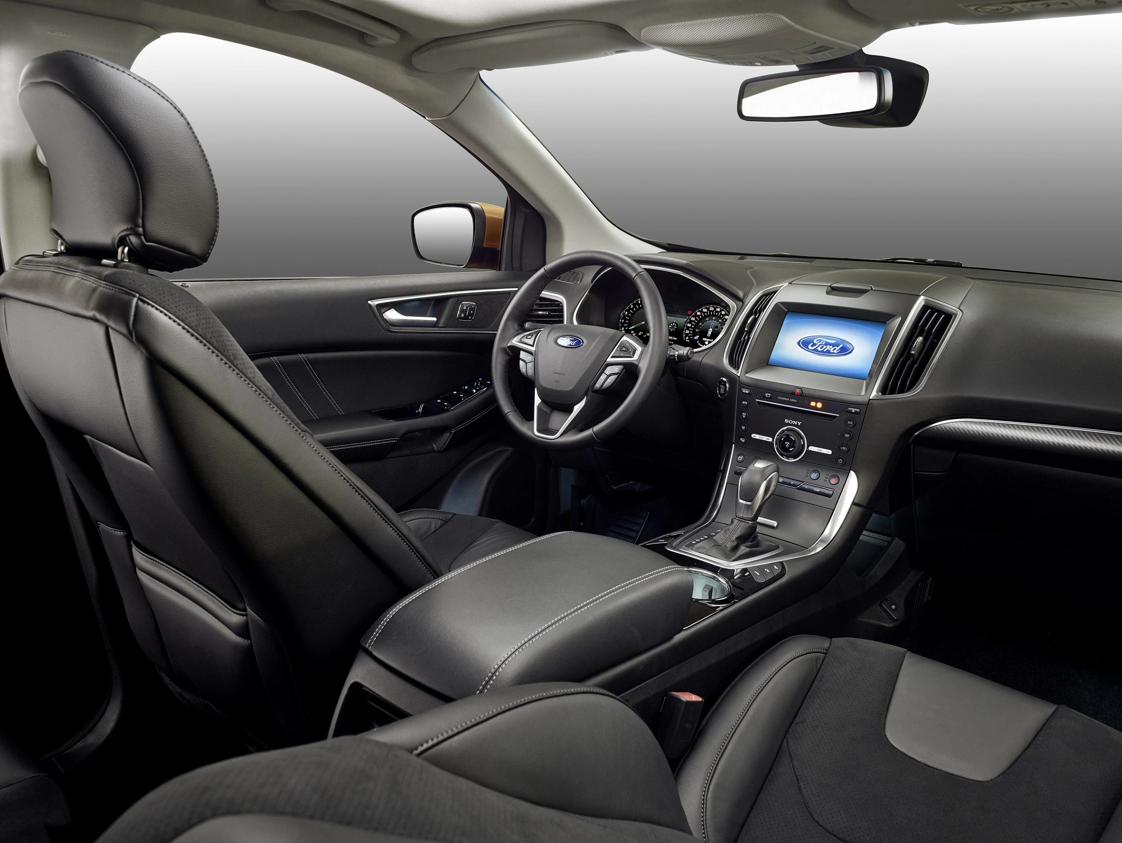 Innenraum eines Autos mit Lederpolstern, Lenkrad, Schalthebel und großem Display auf der Mittelkonsole, modern und sauber gestaltet.