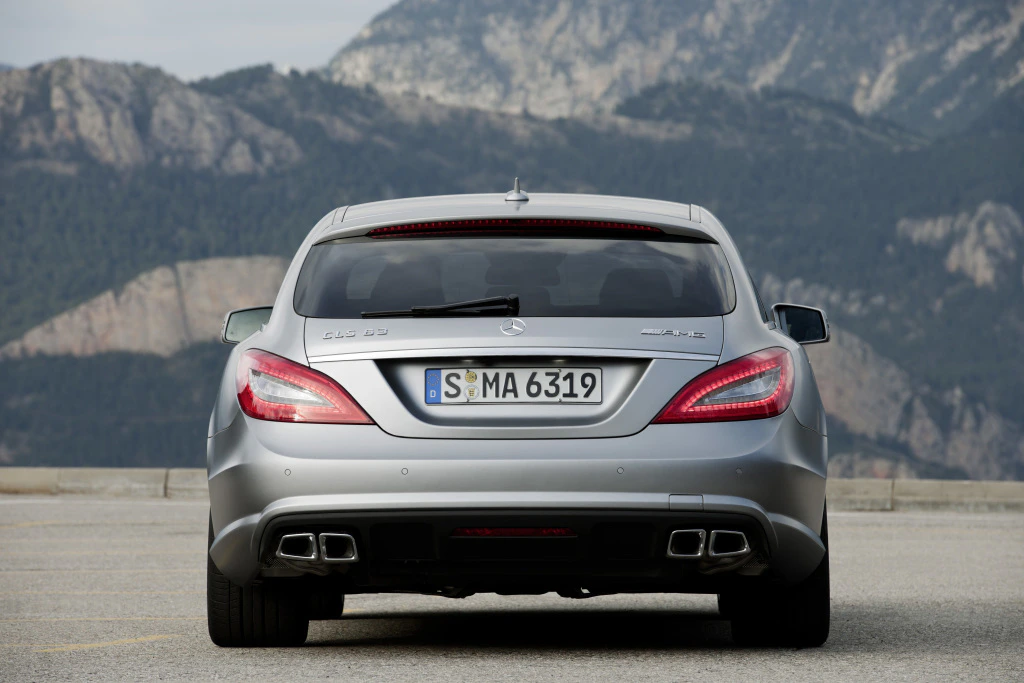 Silberner Mercedes-Benz CLS 63 AMG von hinten, geparkt vor einer Bergkulisse. Heckdesign und Auspuffanlagen sind sichtbar.