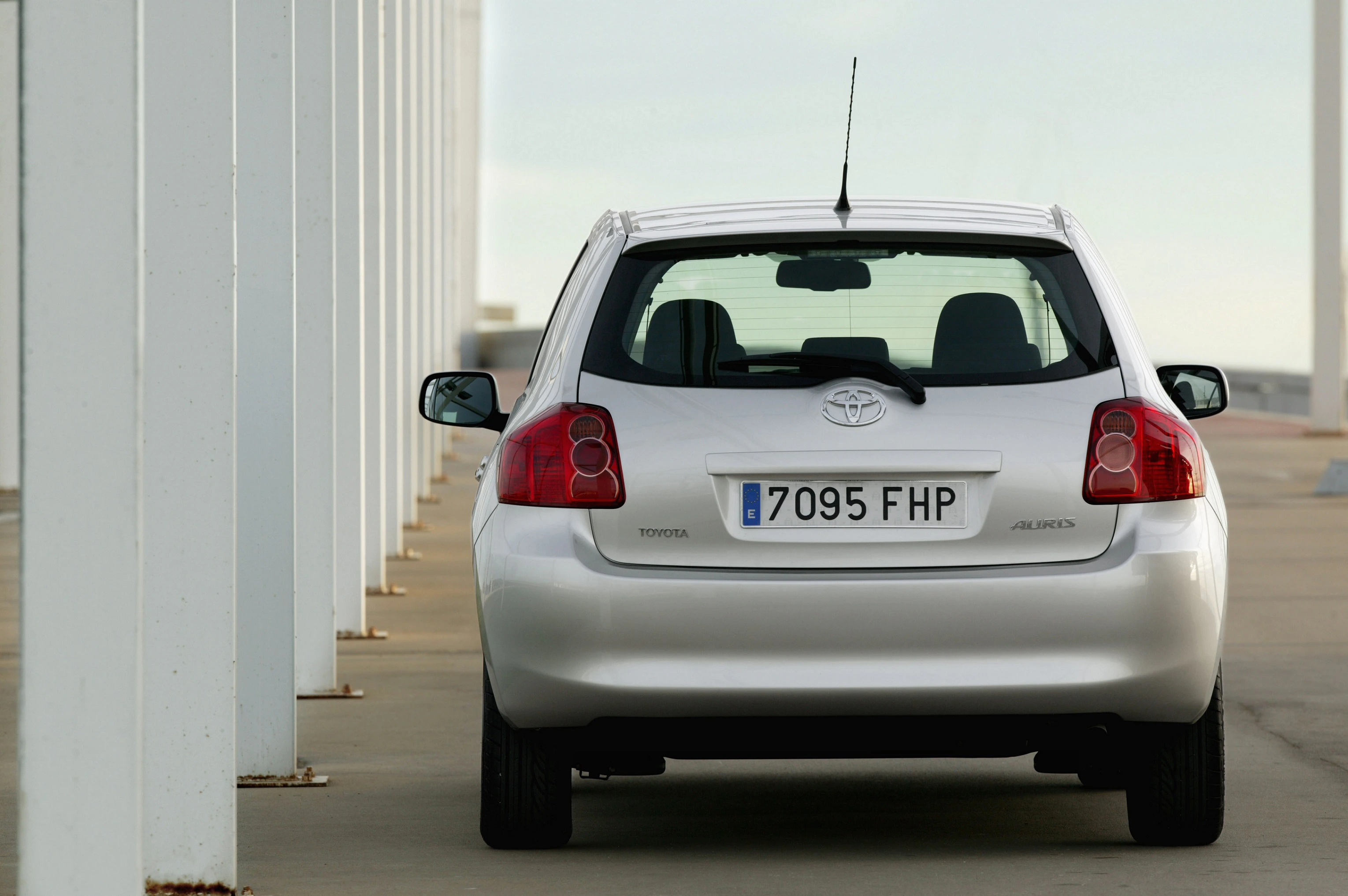 Silberner Toyota Auris von hinten, geparkt auf einem Betonboden neben weißen Säulen, mit spanischem Nummernschild.