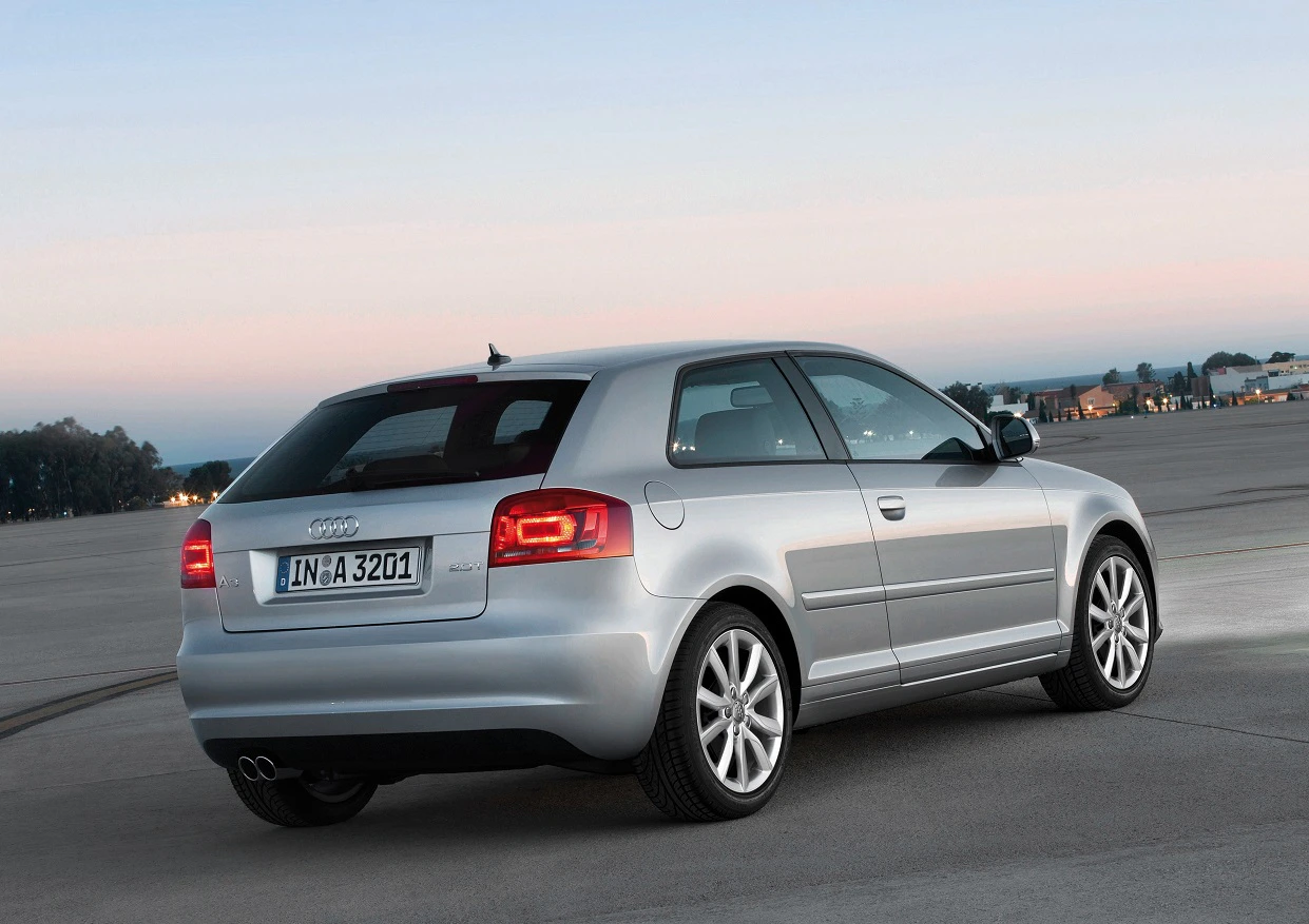 Silberner Audi A3 vor einem Weitblick bei Sonnenaufgang auf einem leeren Parkplatz geparkt, mit sichtbaren Rückleuchten und Auspuff.