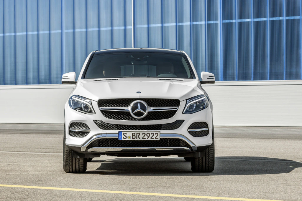 Frontansicht eines weißen Mercedes-Benz SUV vor blauer Glasfassade auf einem Parkplatz.