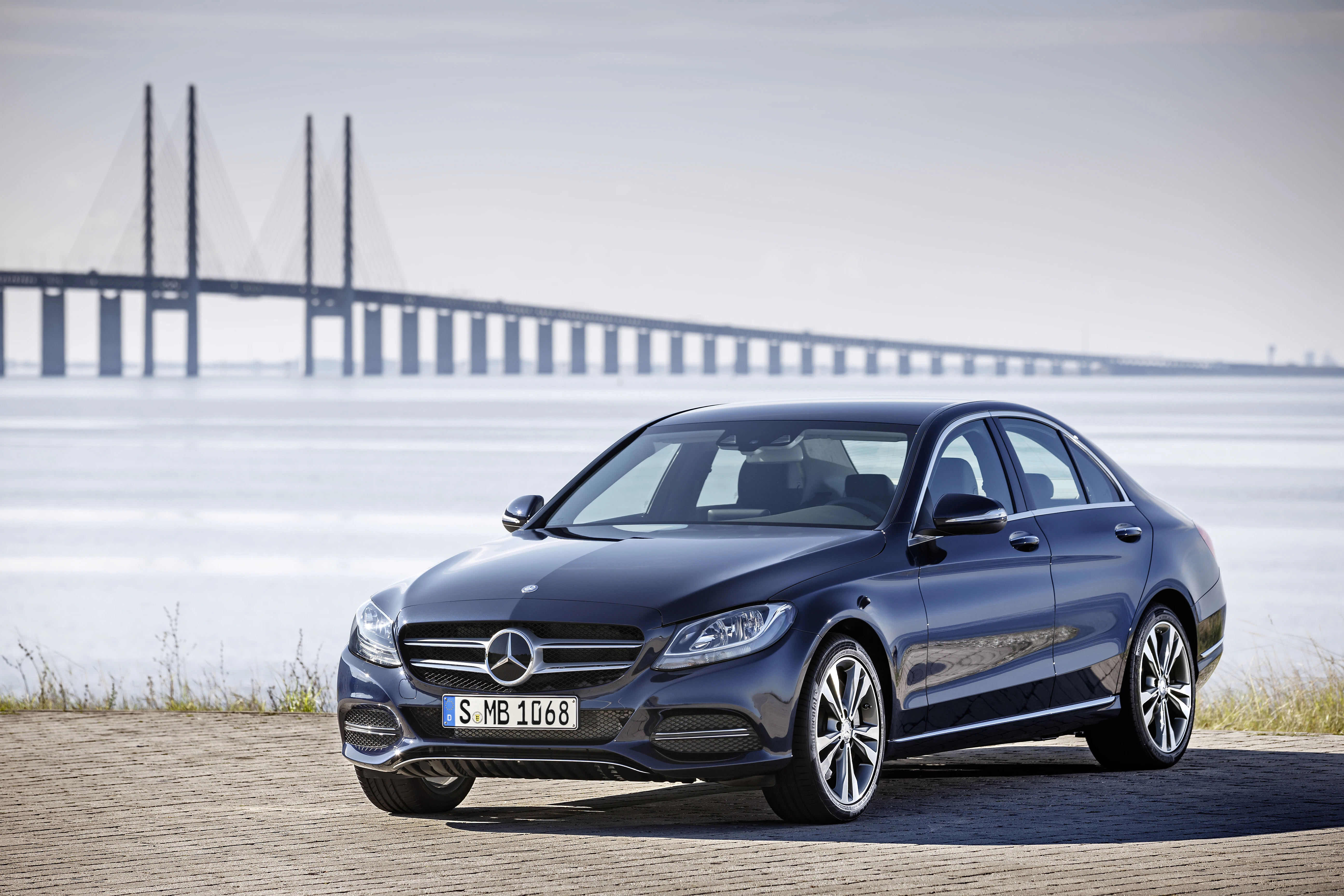 Ein schwarzer Mercedes-Benz steht vor einer Brücke und einem See bei klarem Himmel.