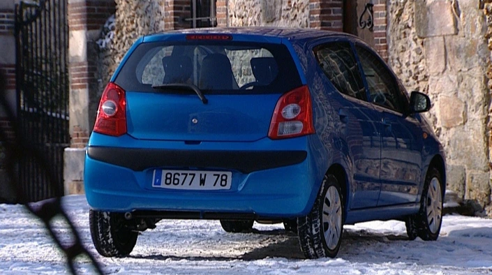 Blauer Kleinwagen parkt im Schnee vor einem Gebäude aus Ziegel und Stein. Französisches Nummernschild sichtbar.