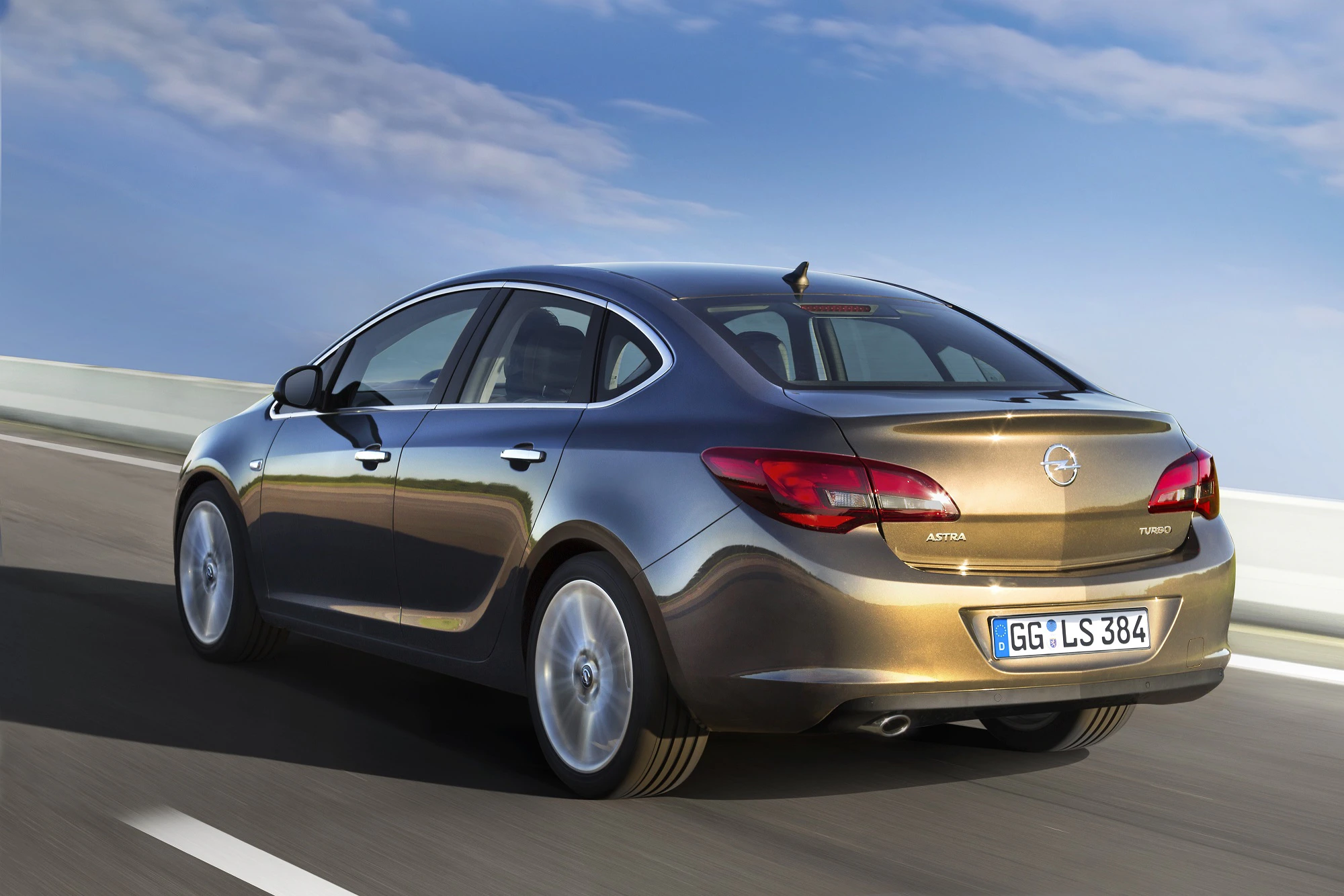 Ein brauner Opel Astra fährt auf einer Autobahn bei sonnigem Wetter. Der Hintergrund zeigt einen blauen Himmel mit vereinzelten Wolken.