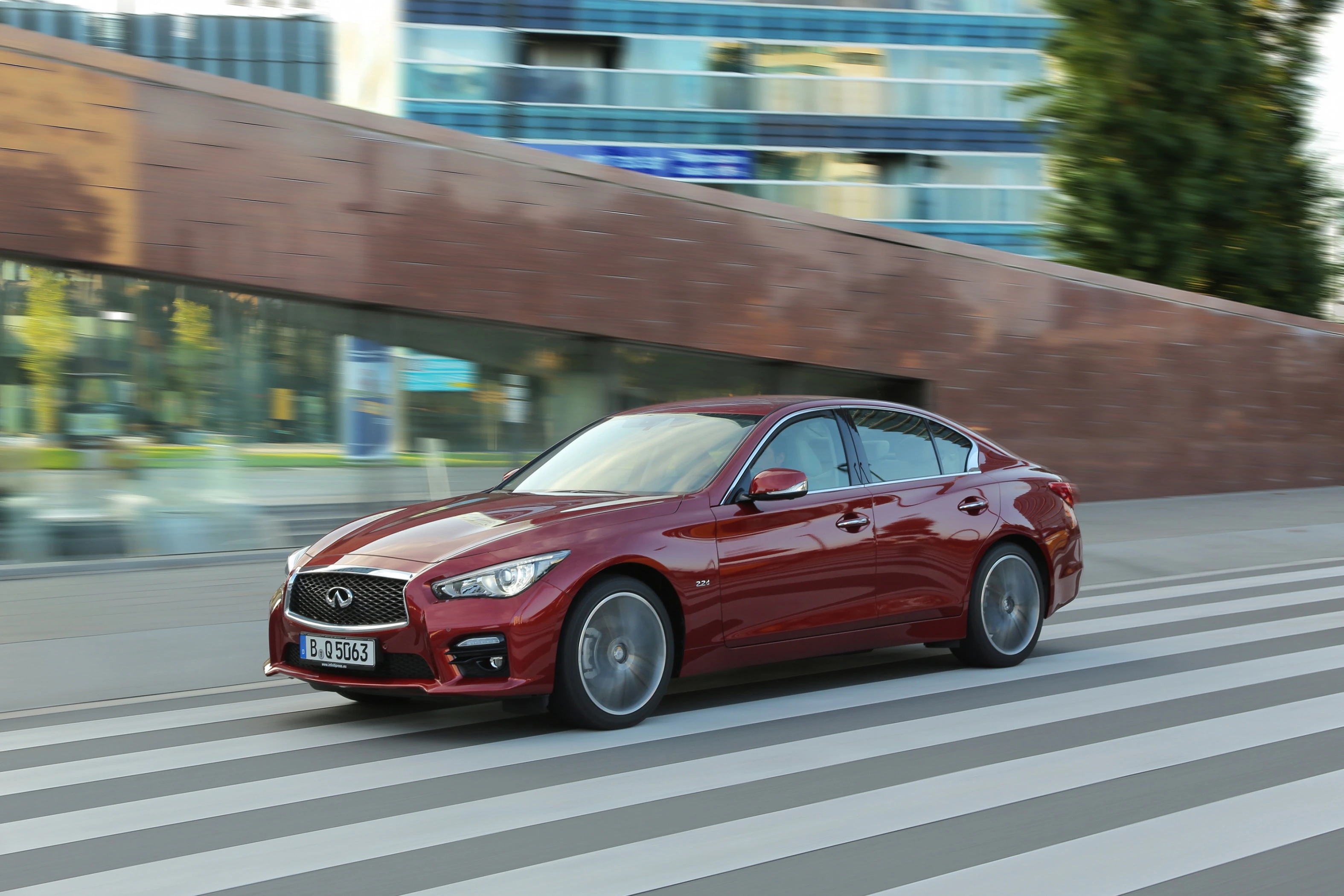 Roter Sportwagen fährt bei Tageslicht auf einer breiten Straße vor modernen Gebäuden.