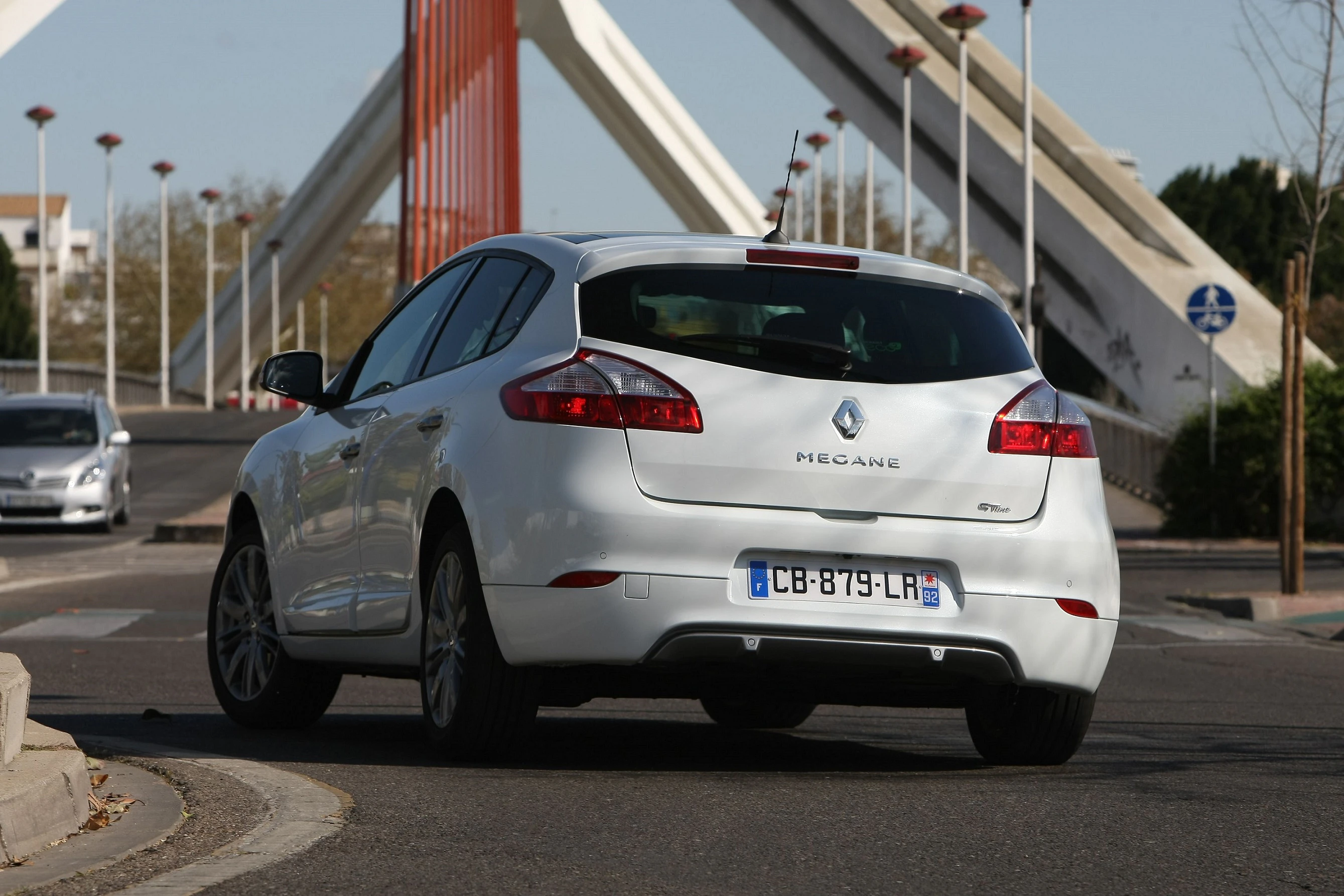 Silberner Renault Mégane fährt auf einer urbanen Straße unter einer modernen Brücke bei Tageslicht.