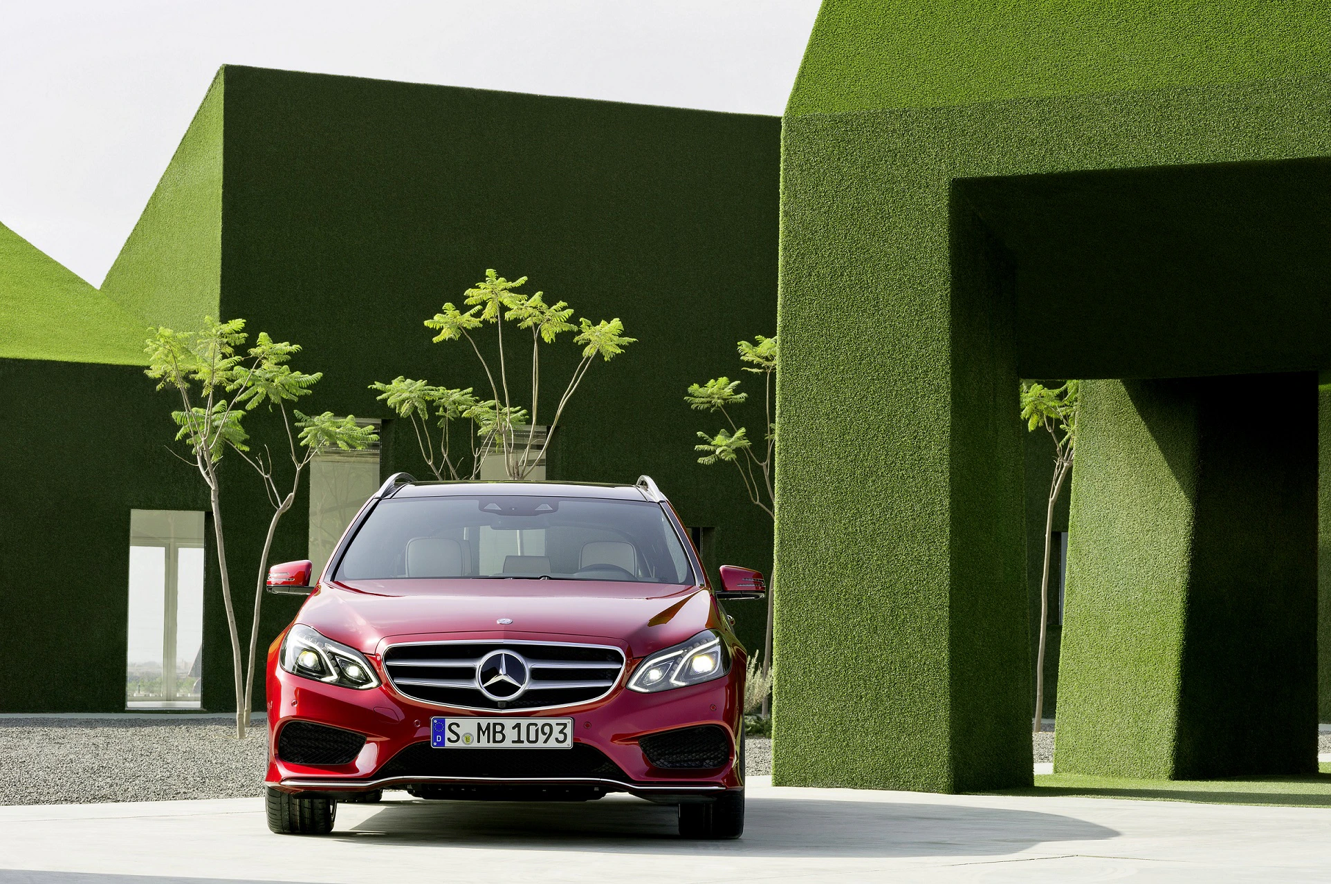 Roter Mercedes-Benz parkt vor modernem Gebäude mit grüner Fassade und Bäumen im Hintergrund.