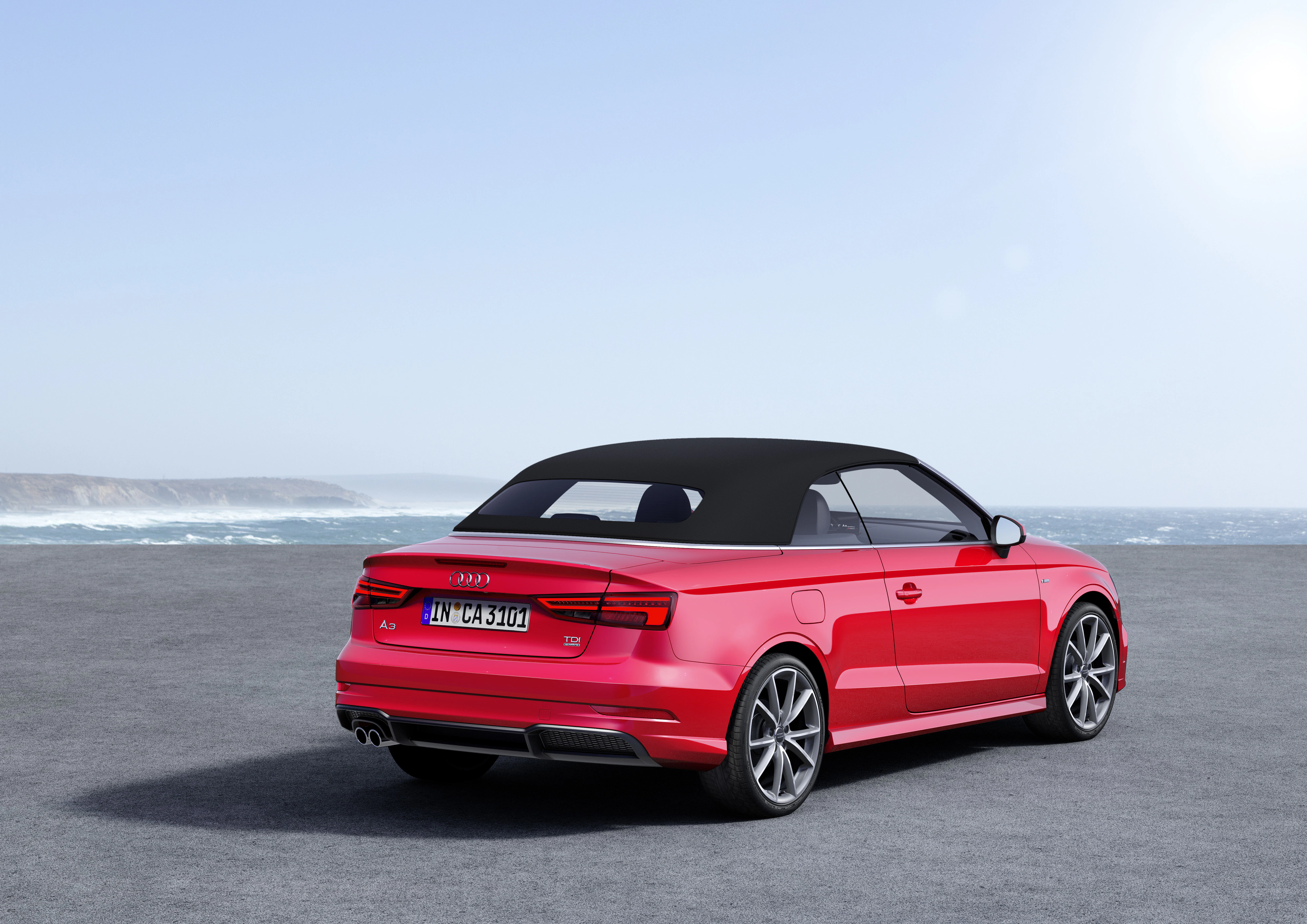 Rotes Cabriolet mit schwarzem Dach steht auf einer Straße vor einem Meereshintergrund bei klarem Himmel.