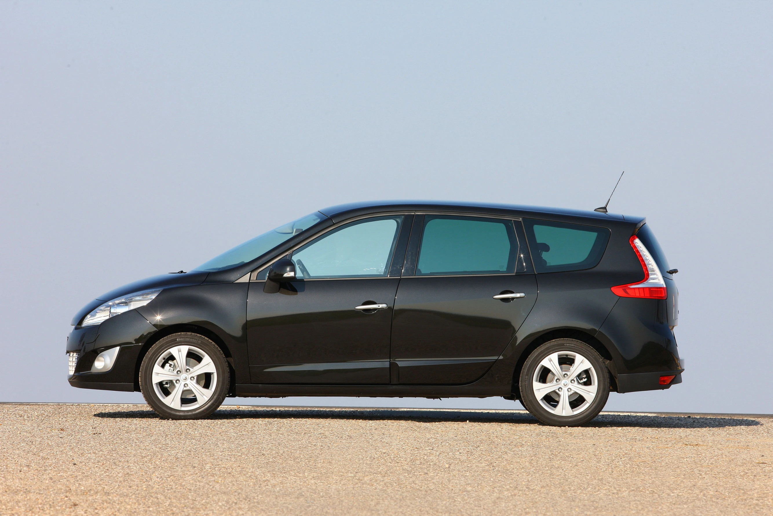 Schwarzer Minivan auf sandigem Untergrund vor blauem Himmel, seitliche Ansicht.