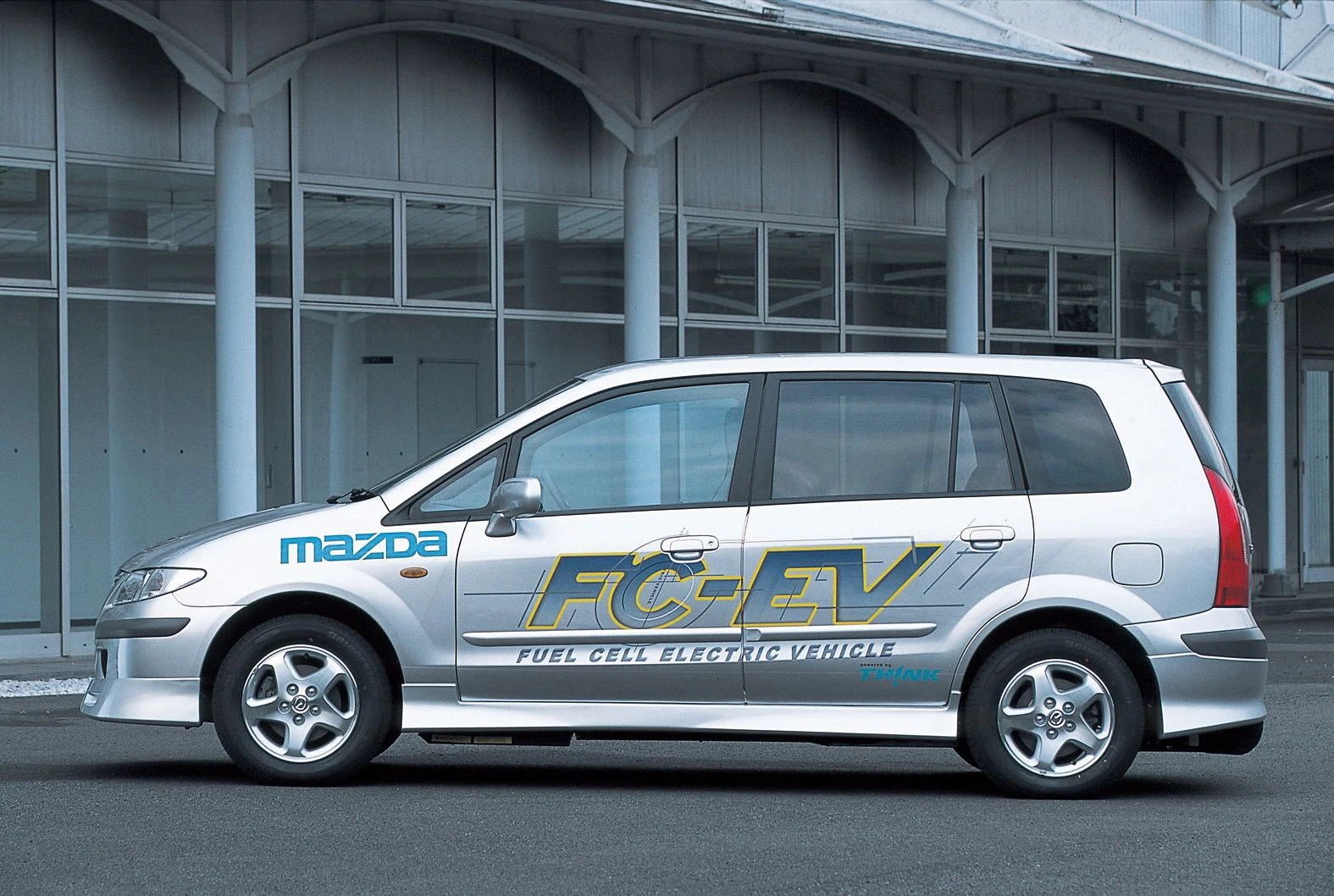 Silberner Mazda FC-EV, mit Wasserstoff-Brennstoffzellen, vor einem modernen Gebäude geparkt.