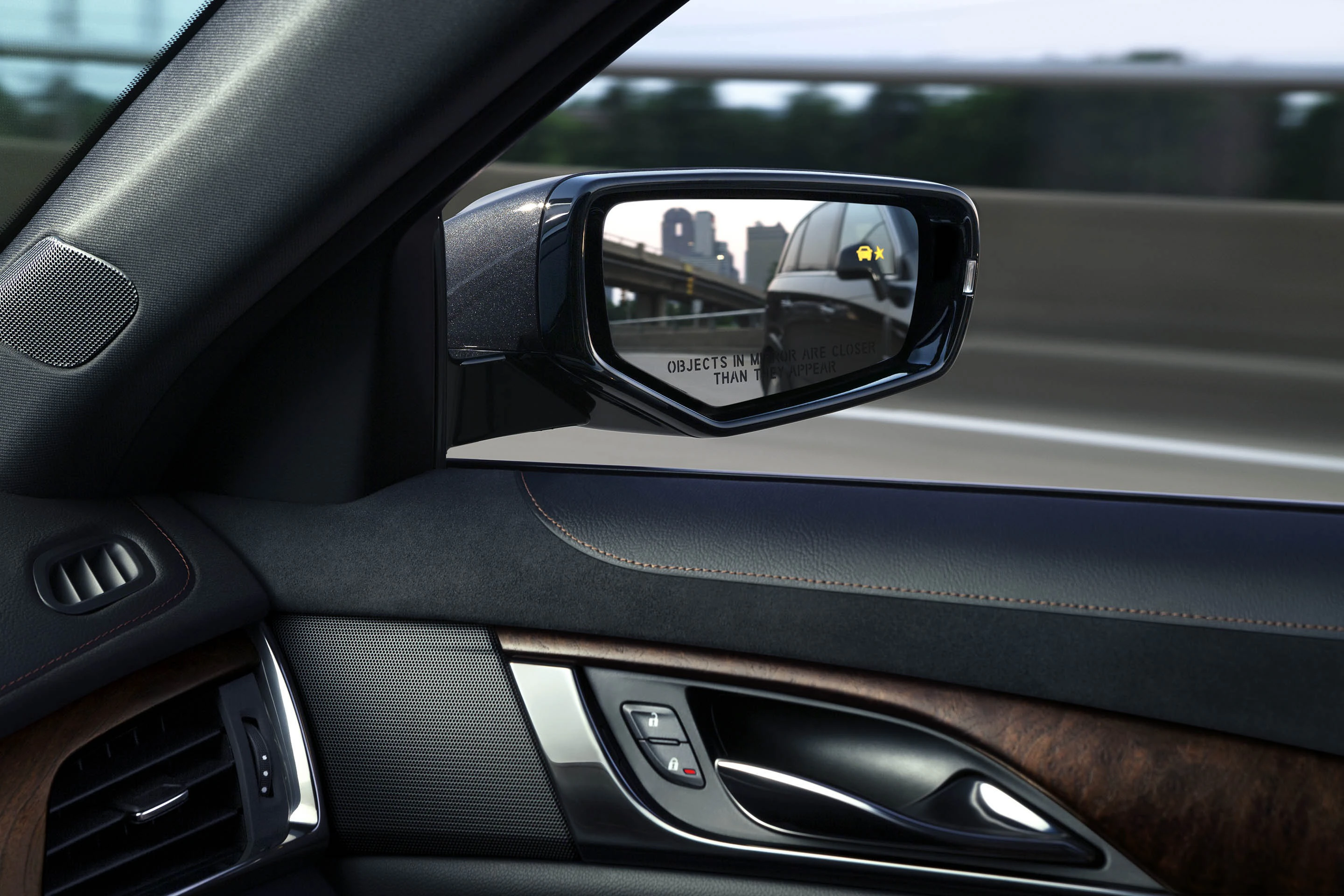 Nahaufnahme eines Autospiegels mit gelber Warnanzeige und einem LKW. Im Hintergrund ist eine unscharfe Autobahn zu sehen.