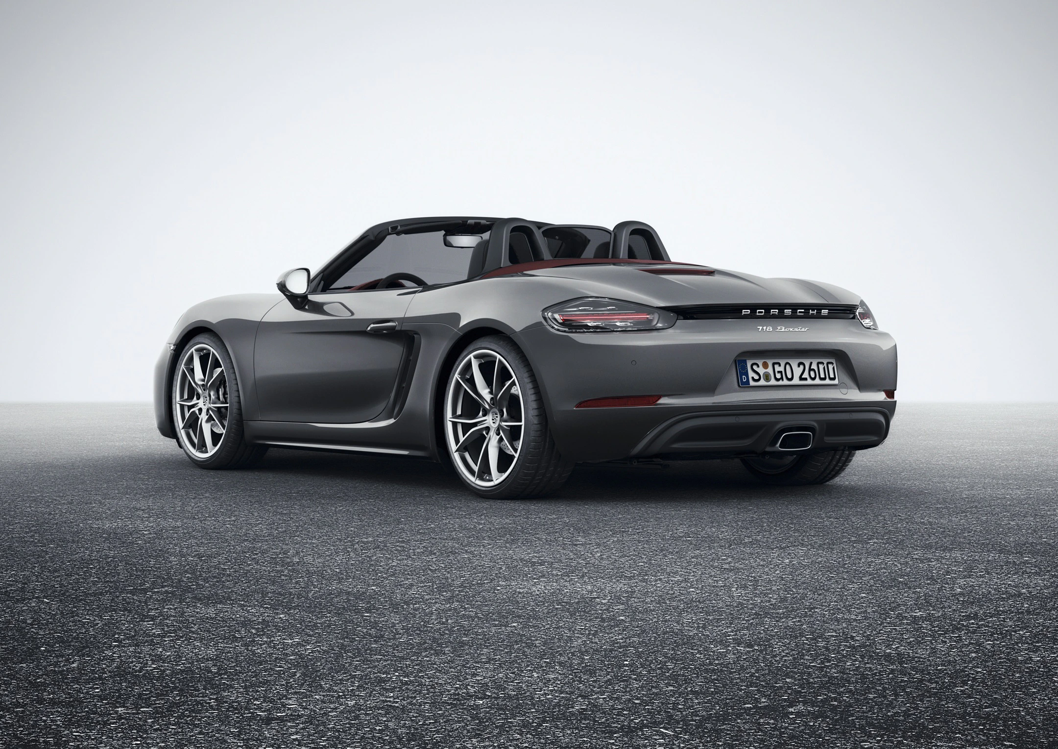 Grauer Sportwagen, Porsche 718 Boxster, auf einer grauen Fläche. Cabrio-Verdeck offen, modernes Design. Lizenznummer sichtbar.