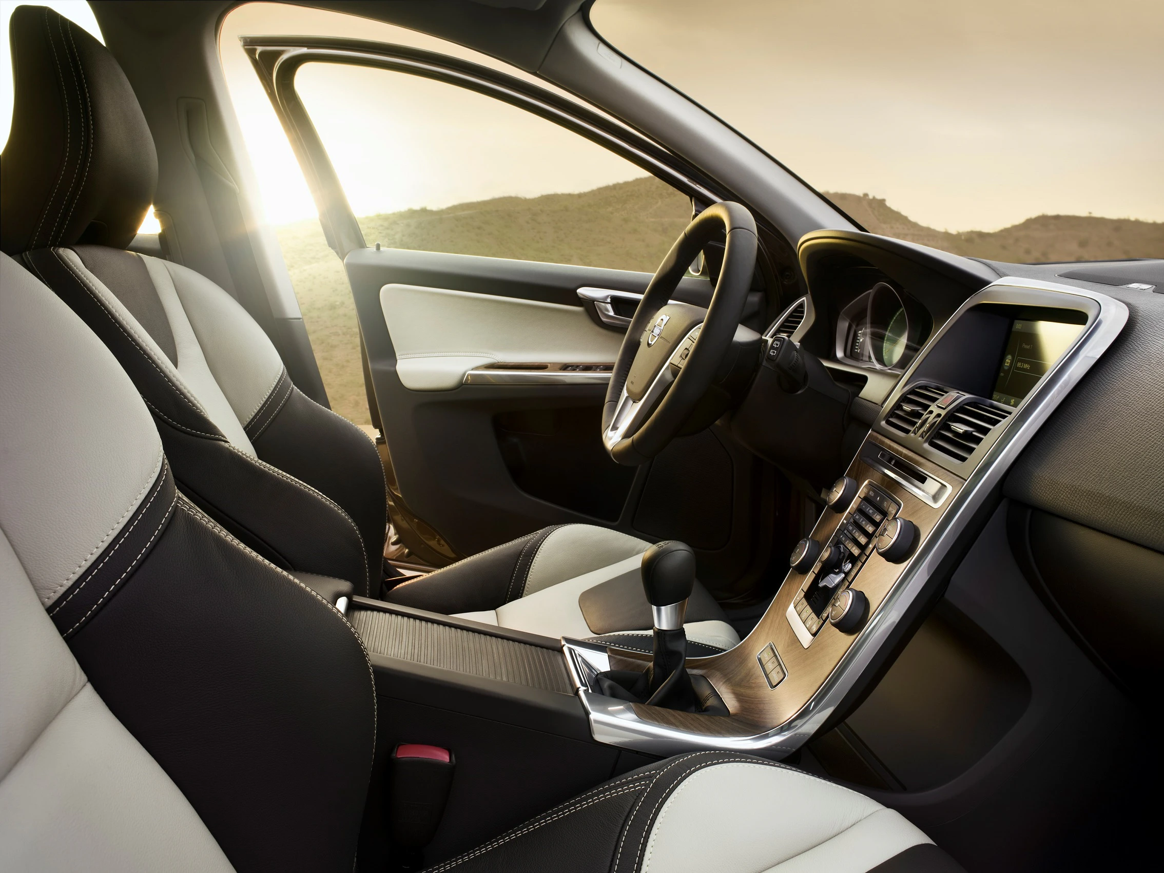 Innenraum eines modernen Autos mit zweifarbigem Leder, elegantem Armaturenbrett und offener Fahrertür, im Hintergrund eine Landschaft bei Sonnenuntergang.