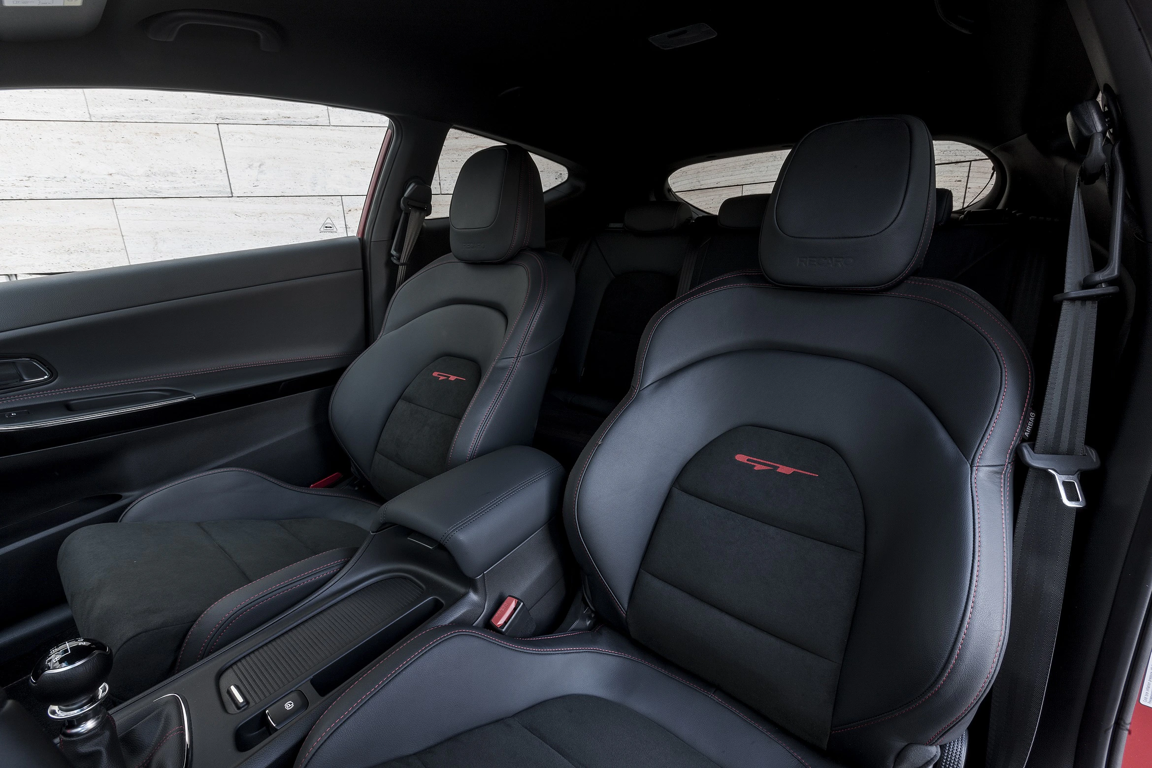 Innenraum eines Autos mit schwarzen Ledersitzen und roten Nähten. Die Sitze sind sportlich gehalten, Armlehne und Konsole sichtbar.