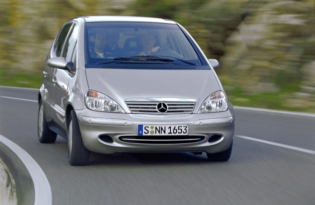 Silberner Mercedes-Benz A-Klasse fährt auf kurviger Landstraße. Hintergrund verschwommen, Auto frontal fotografiert.