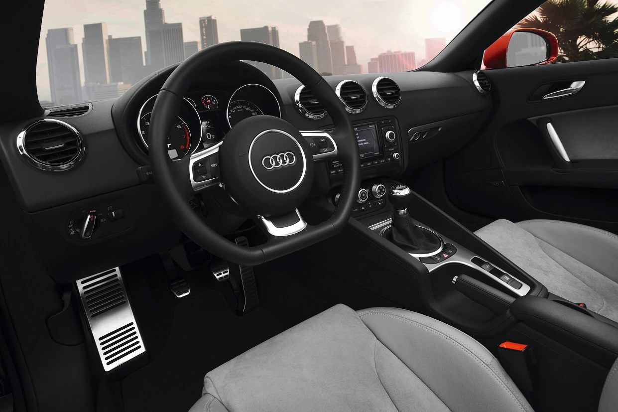 Innenraum eines Audi mit schwarzem Armaturenbrett, modernem Lenkrad und heller Lederausstattung; Skyline im Hintergrund sichtbar.