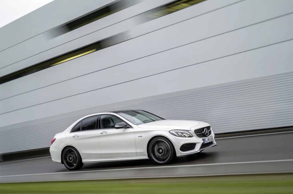 Weißer Mercedes-Benz fährt dynamisch auf Straße vor moderner, grauer Gebäudewand.