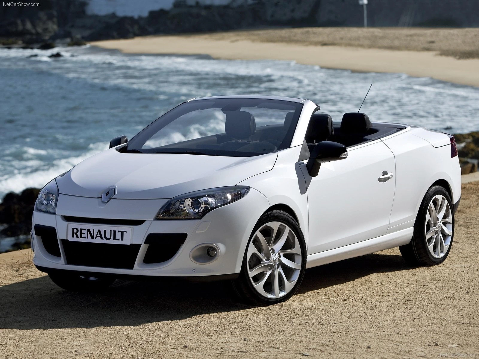 Ein weißer Renault Cabriolet steht vor einer Küstenlandschaft mit Sandstrand und Meer im Hintergrund.