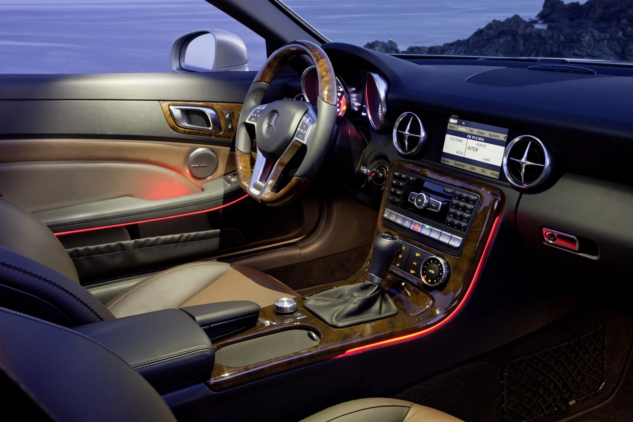 Innenraum eines luxuriösen Autos mit Ledersitzen, Holzverkleidung, beleuchtetem Armaturenbrett und modernem Infotainment-System bei Nacht.