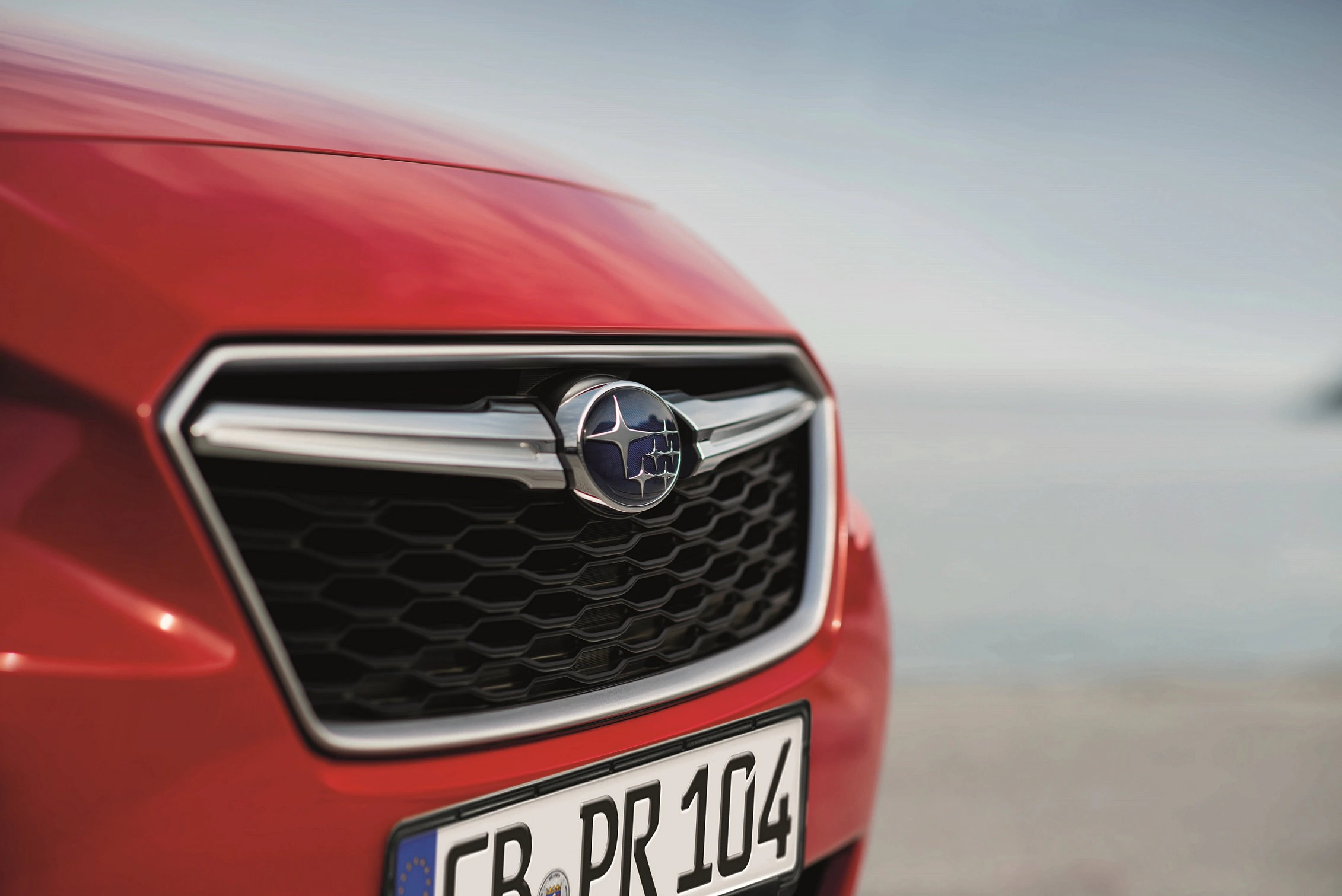 Nahaufnahme eines roten Subaru mit sichtbarem Logo und deutschem Nummernschild vor einem unscharfen Hintergrund.