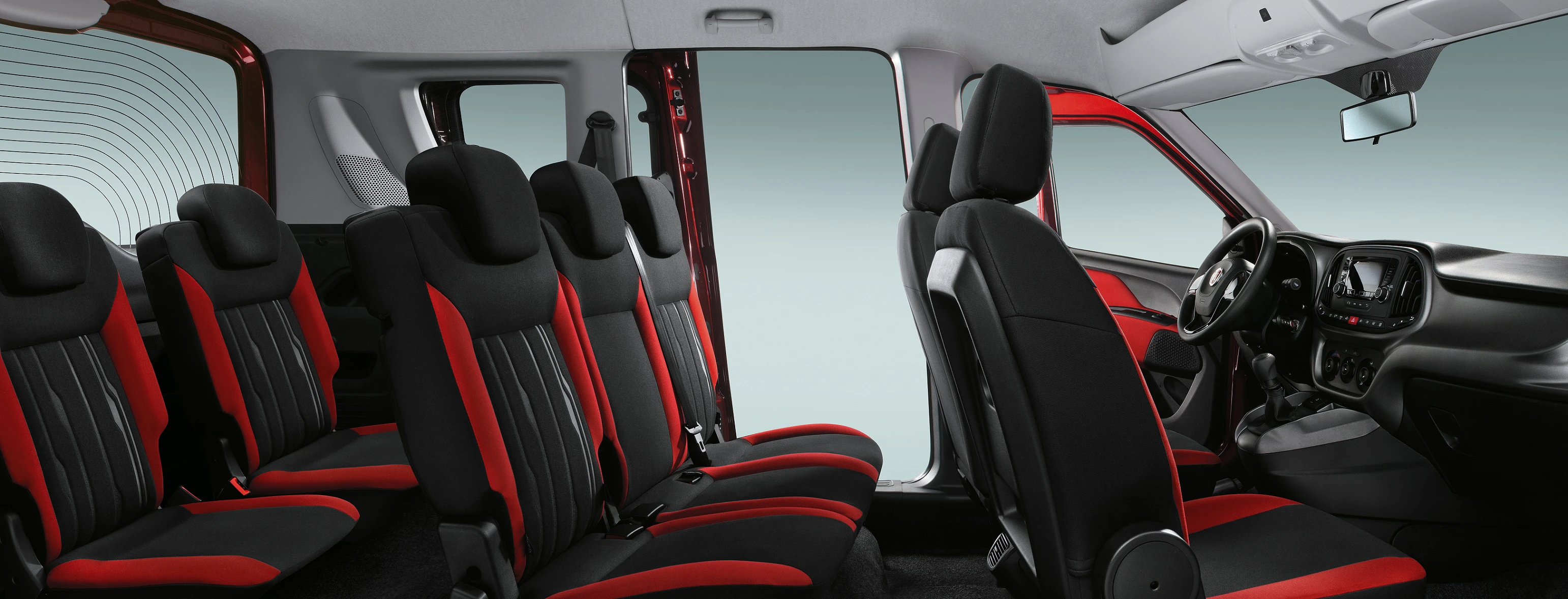 Innenraum eines Vans mit sieben schwarzen und roten Sitzen. Sicht auf Fahrer- und Beifahrersitz, sowie zweite und dritte Sitzreihe.