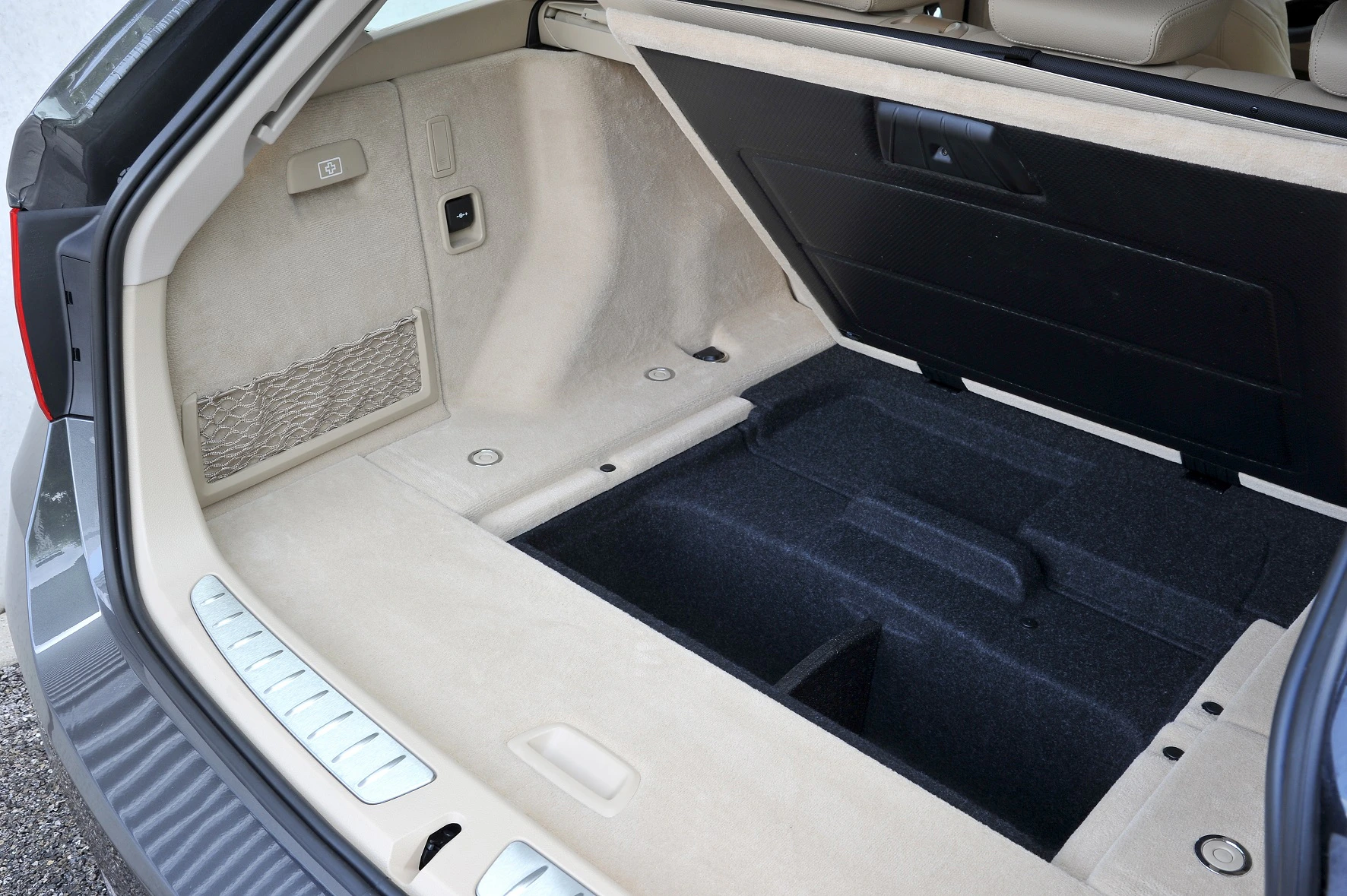 Der geöffnete Kofferraum eines Autos zeigt einen geräumigen Innenraum mit hellen Verkleidungen und einem dunklen, gepolsterten Bodenbereich.