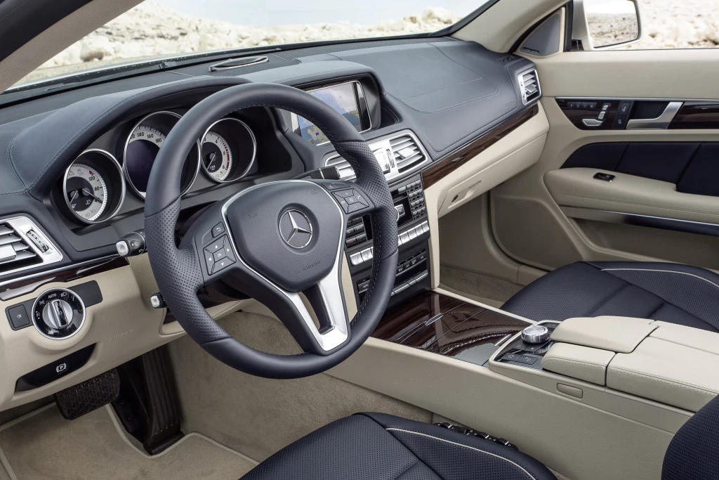 Innenraum eines modernen Mercedes mit Lederlenkrad, digitalem Display und eleganten beigen und schwarzen Ledersitzen.