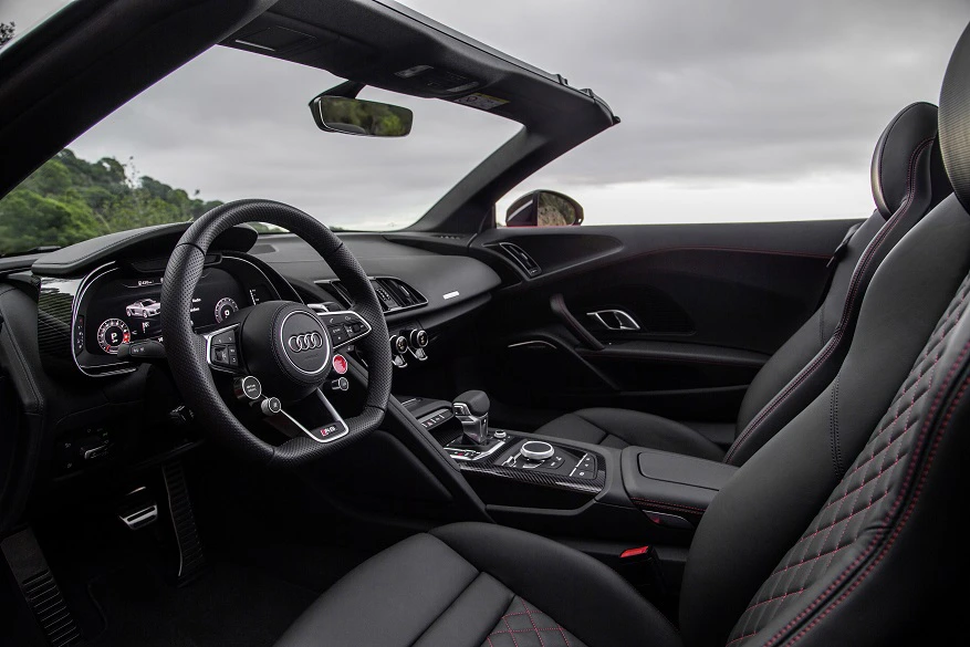 Innenraum eines Audis mit sportlichem Design. Schwarze Ledersitze, roter Naht, Lenkrad mit Multifunktionstasten und digitalem Armaturenbrett.