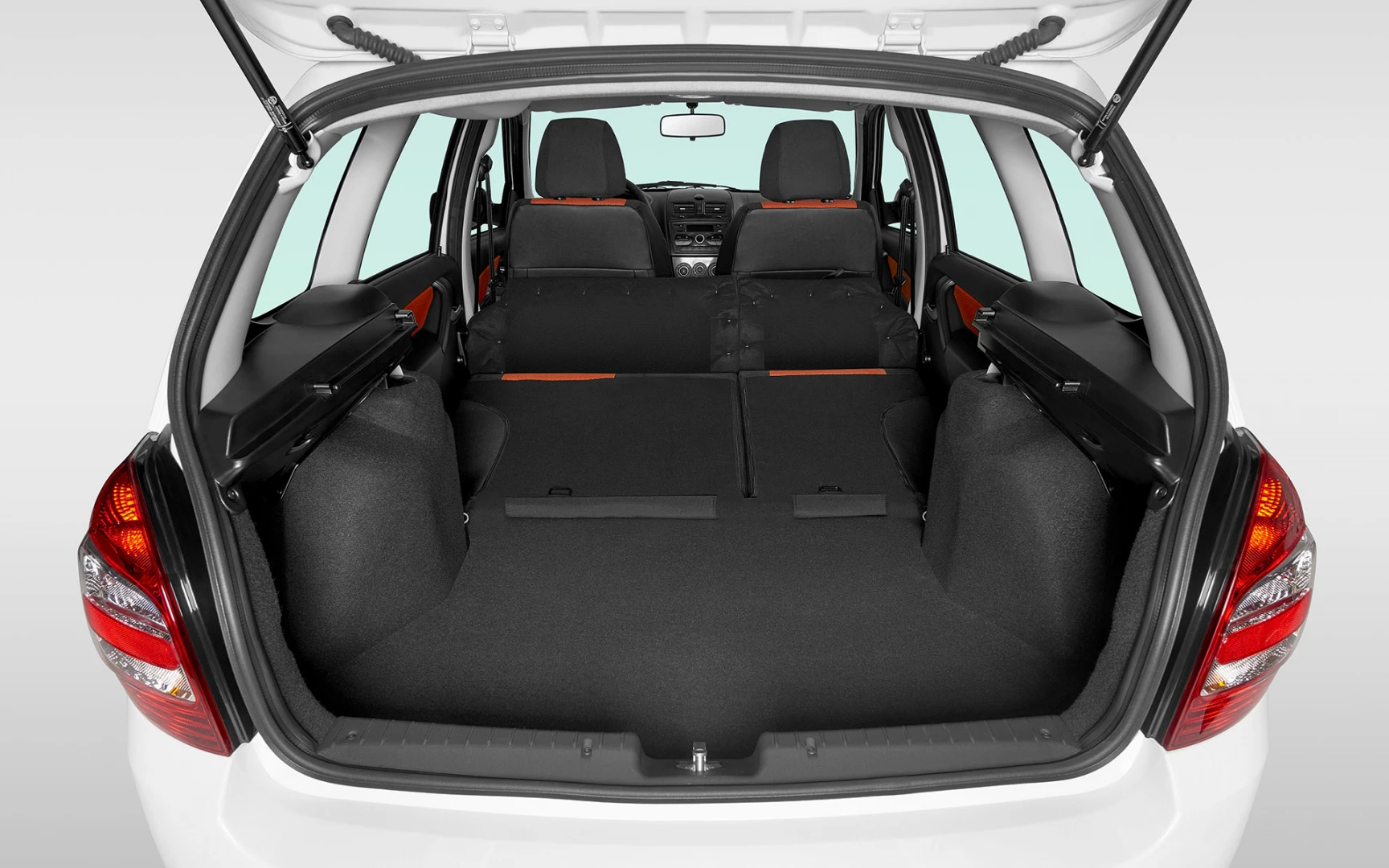 Kofferraum eines Autos mit umgeklappten Rücksitzen, bietet viel Ladefläche. Sitzbezüge in Orange, Cockpit im Hintergrund sichtbar.
