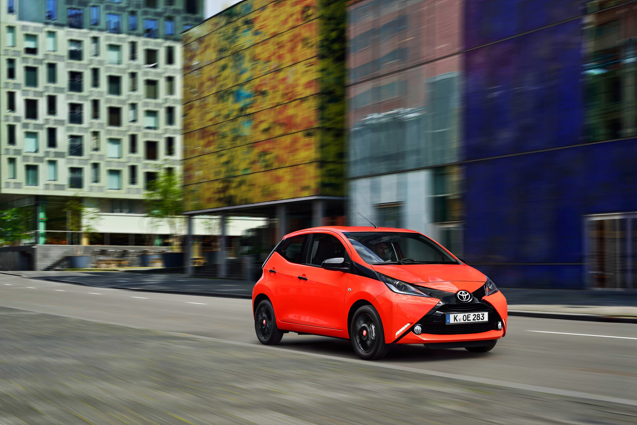 Ein roter Toyota fährt auf einer städtischen Straße mit modernen Gebäuden im Hintergrund.