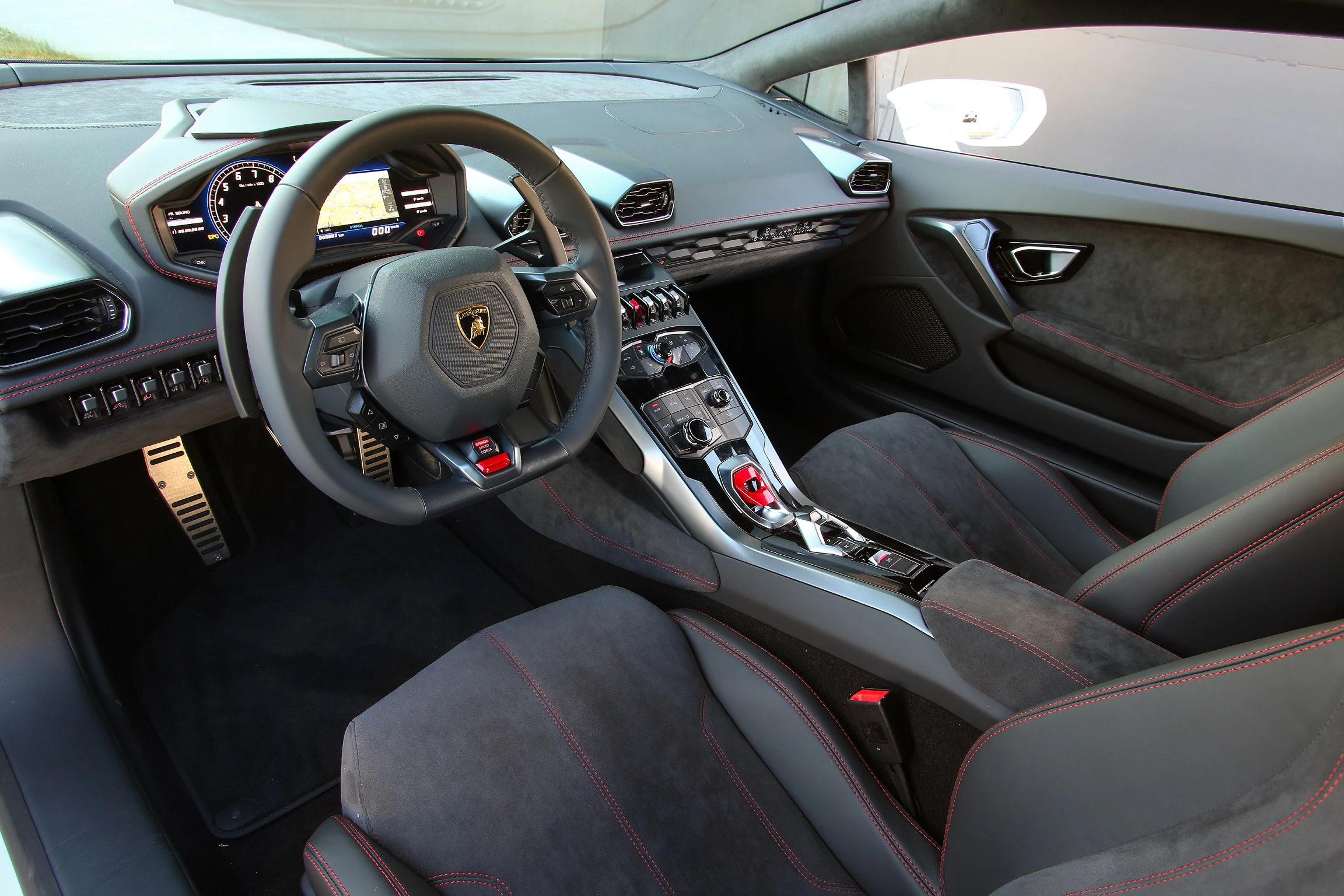 Innenraum eines sportlichen Autos mit modernen Instrumenten, Lederlenkrad und roten Kontrastnähten. Elegante Mittelkonsole mit Touchscreen.