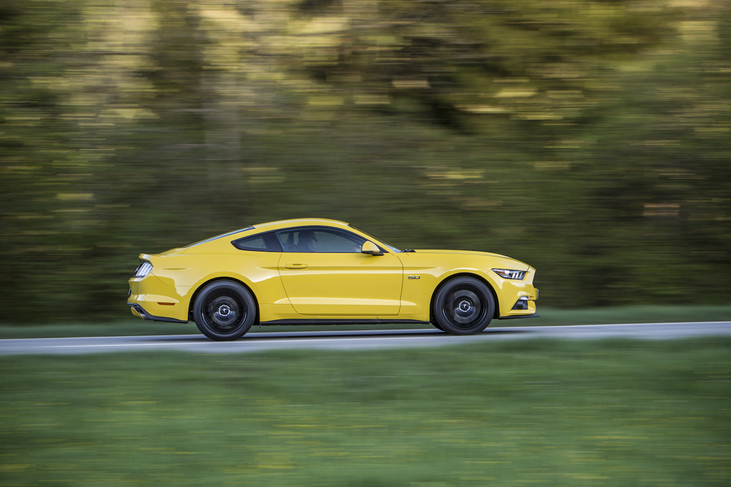 Gelbes Sportauto fährt schnell auf einer Landstraße, grüner Hintergrund ist leicht verschwommen.
