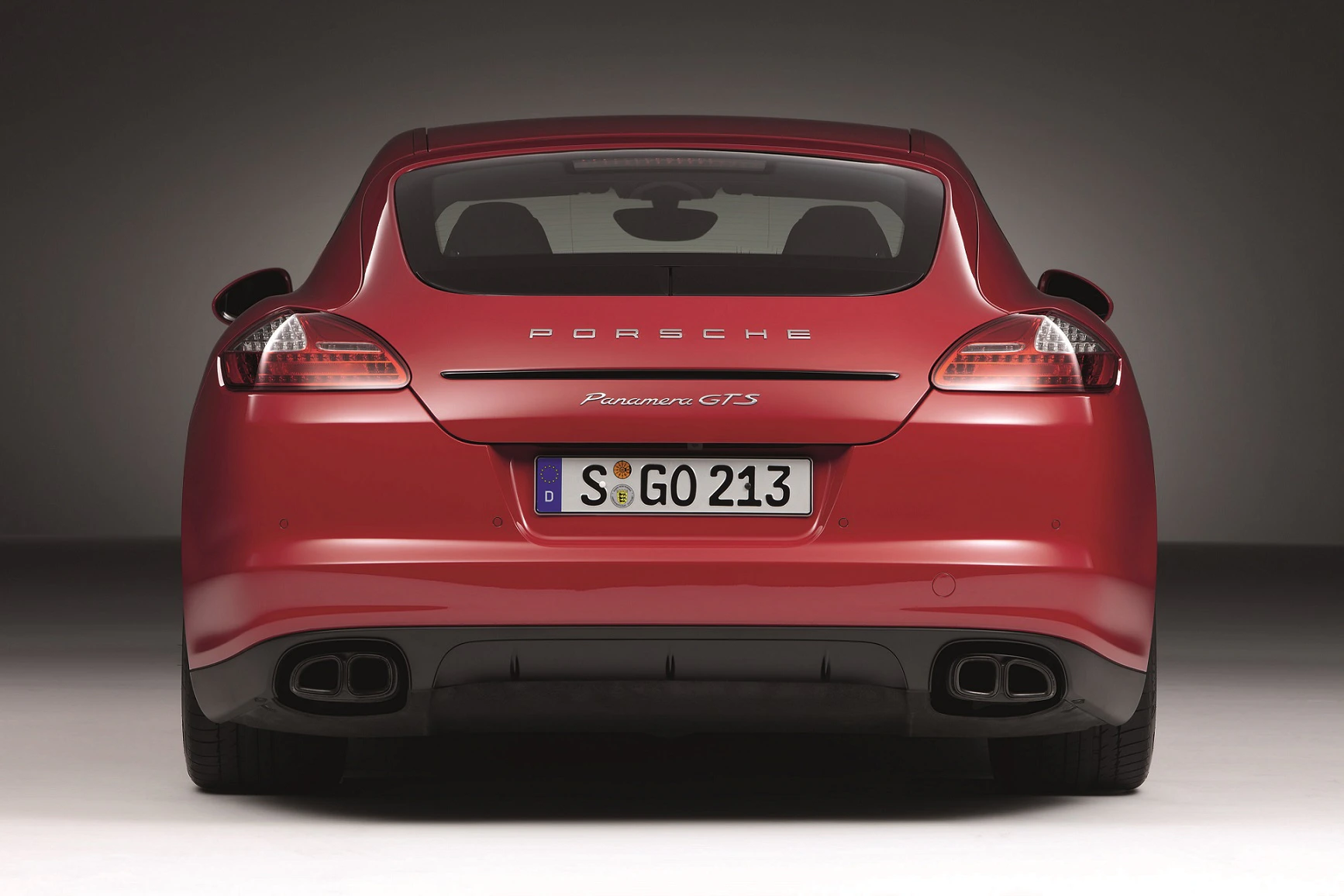Roter Porsche Panamera GTS von hinten, mit sichtbarem Auspuff, Rücklichtern und Nummernschild vor grauem Hintergrund.