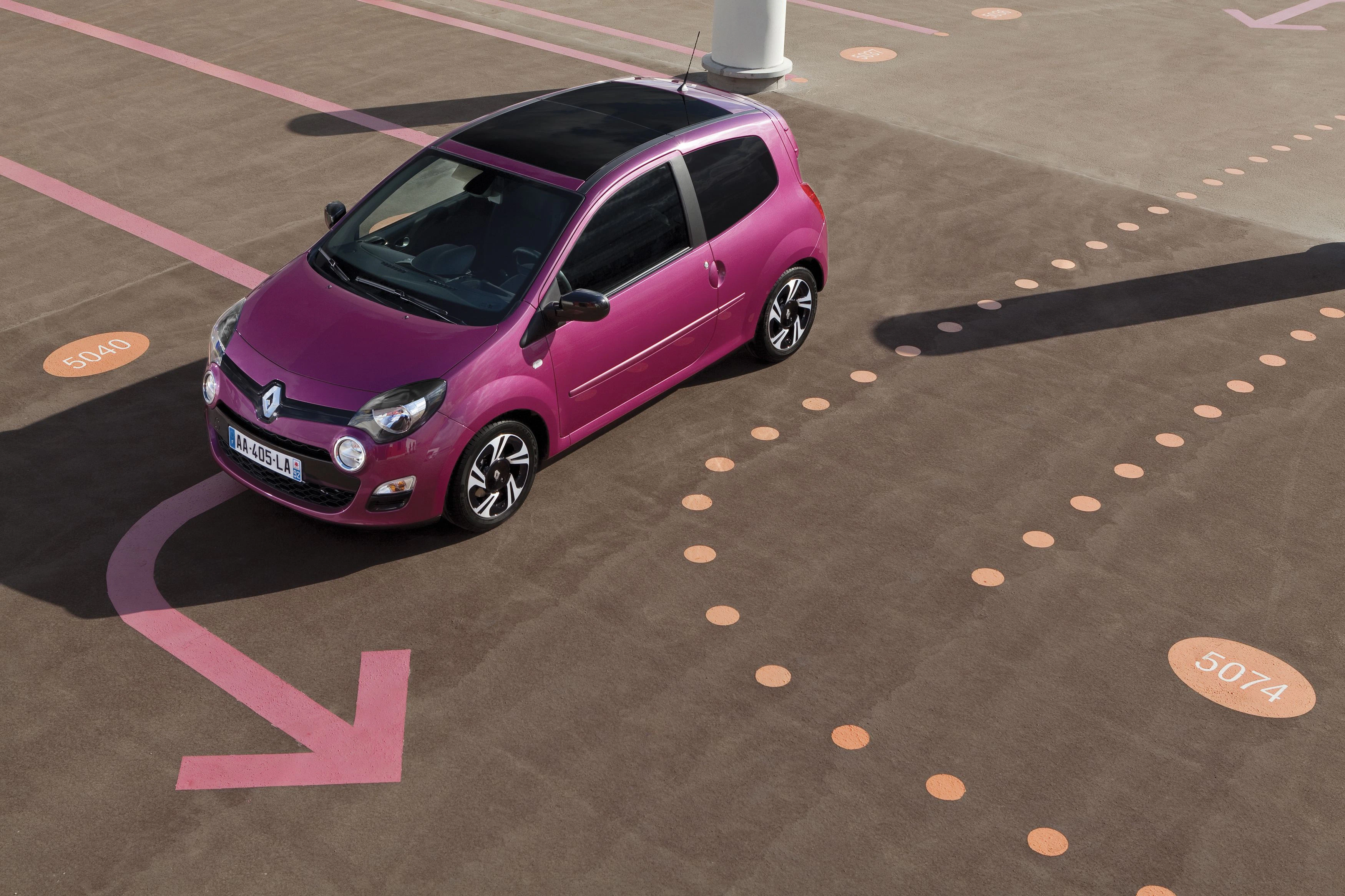Pinkes Auto auf Parkplatz mit rosa Markierungen. Auto zeigt nach vorne, umgeben von nummerierten Kreisen. Sonniger Tag.